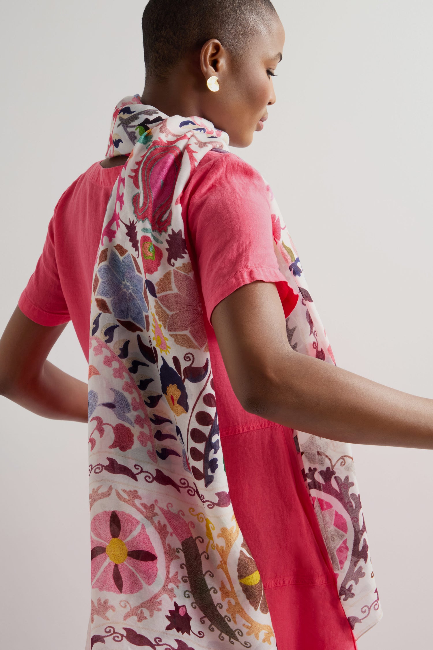 A person wearing a bright pink dress, paired with a Suzani Print Scarf featuring vibrant needlework.
