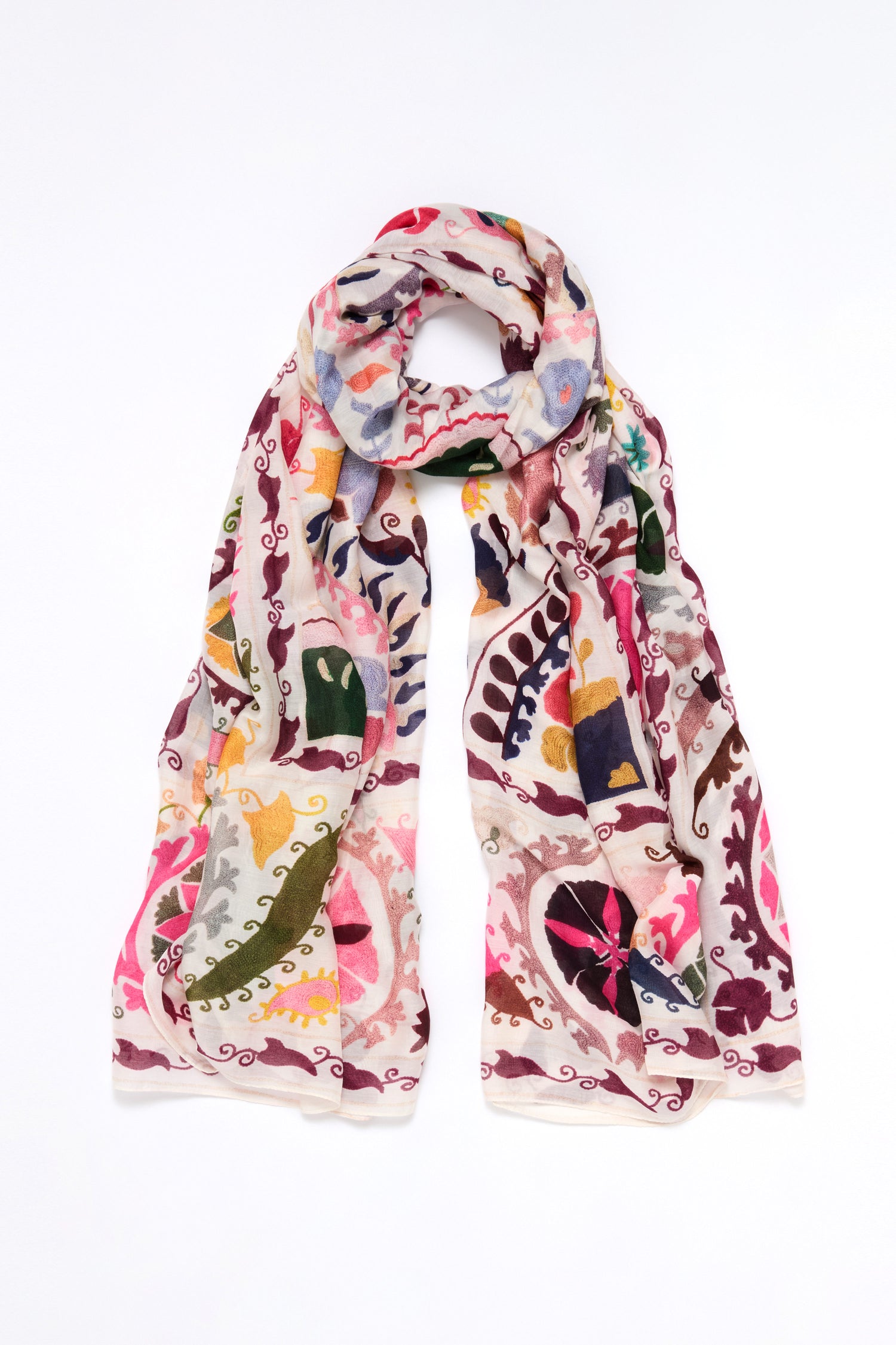 The Suzani Print Scarf boasts a vibrant floral and paisley pattern on a white background, echoing the intricacy of traditional Suzani needlework.