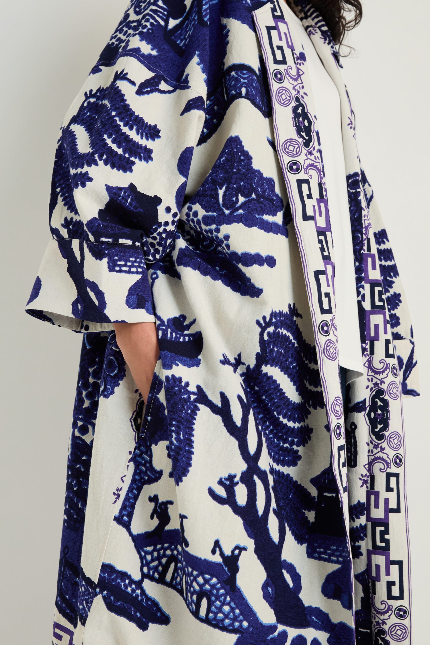 Wearing the Willow Print Summer Coat—loose, lightweight, and adorned with a blue and white landscape design—this piece is perfect for summer layering, featuring side pockets for added style and convenience.