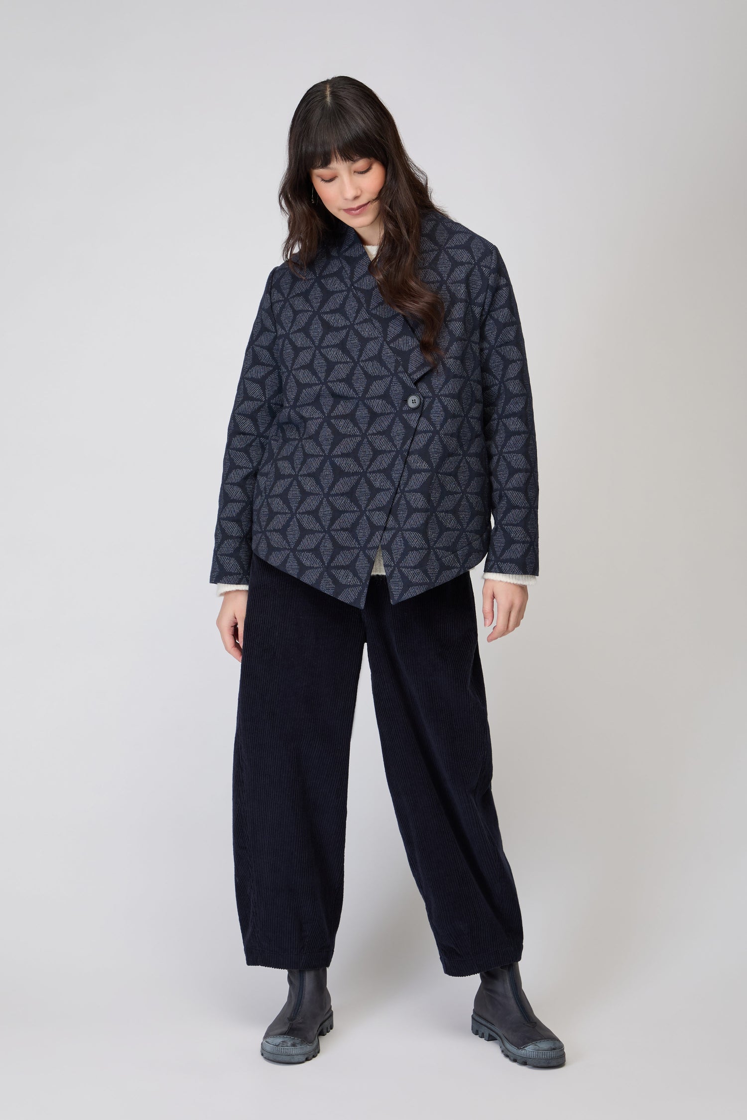 A person wearing a Diamond Floral Indigo Jacket featuring geometric shapes and two buttons stands with one hand on their hip.
