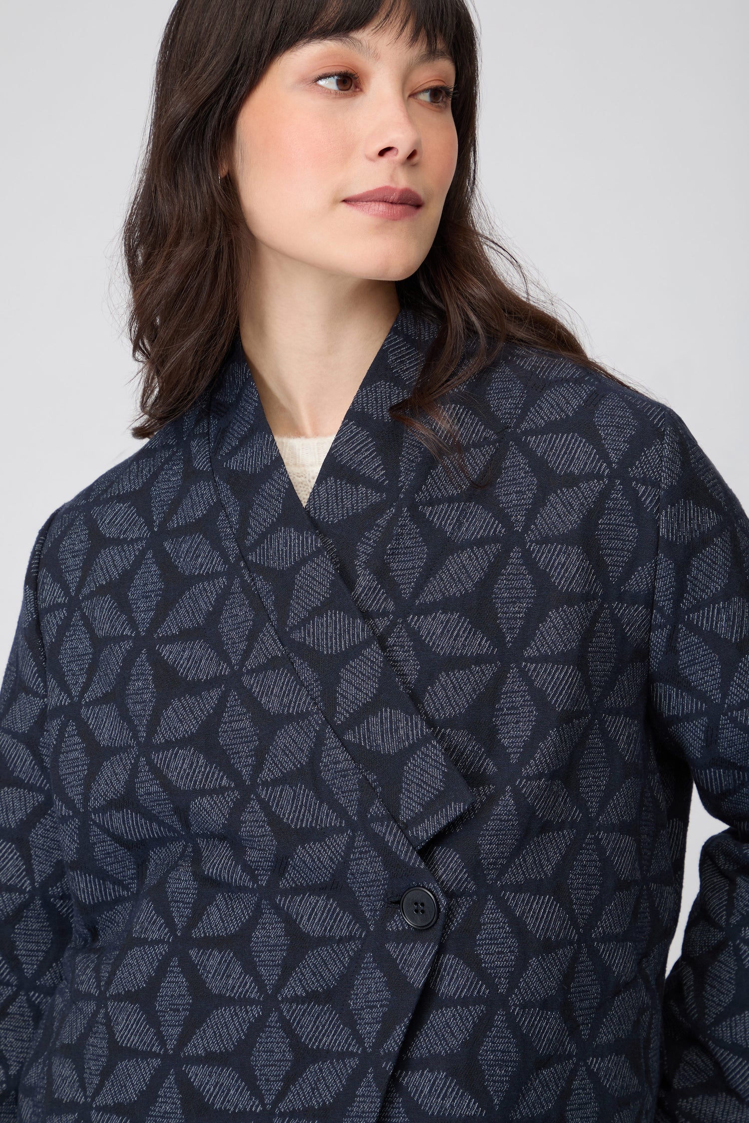 A woman stands against a plain background wearing the Diamond Floral Indigo Jacket, paired with loose navy pants and white sneakers.