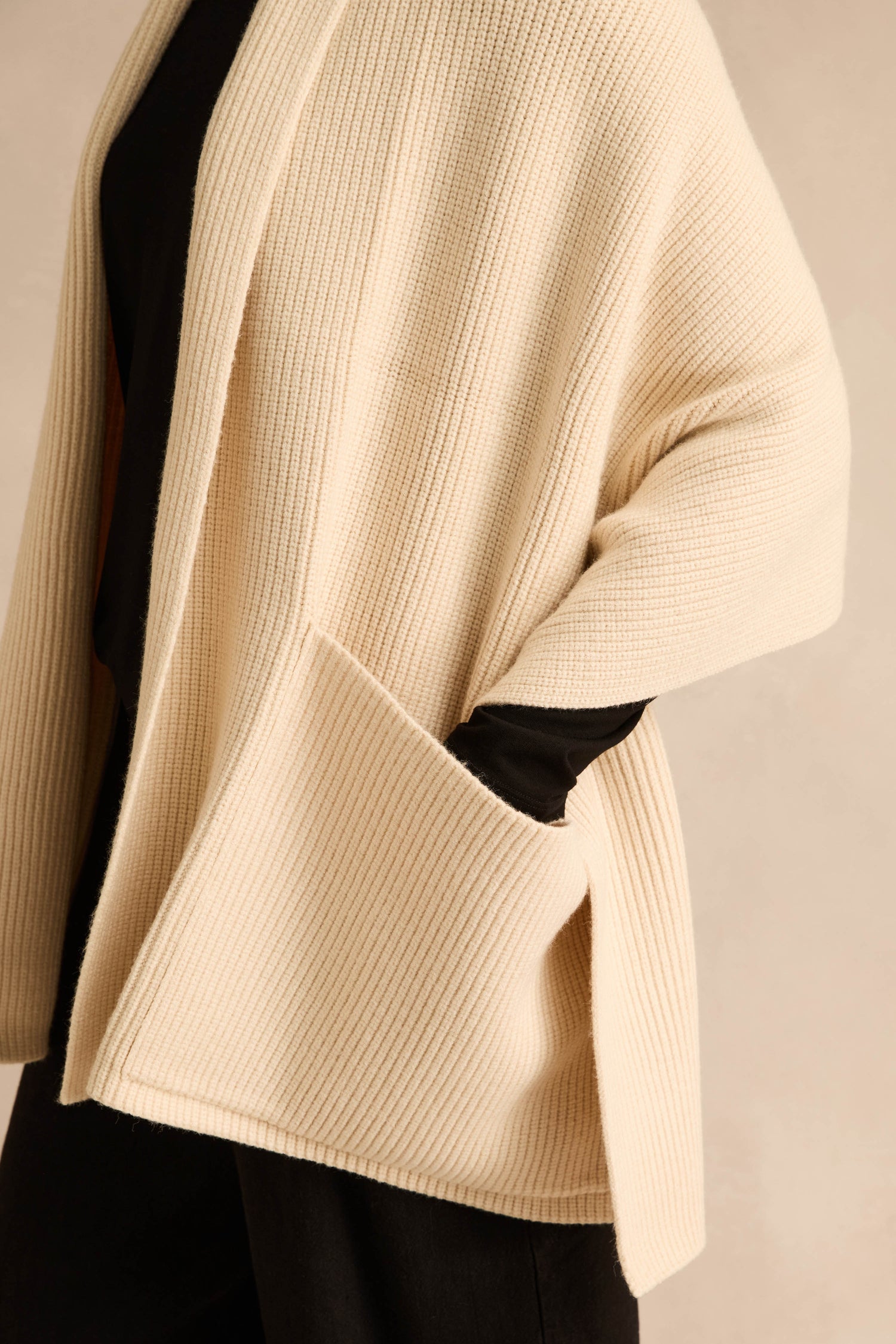 A person wearing the Cream Pocket Scarf—a cream-colored, ribbed knit scarf with oversized pockets—over a black top and black pants, shown from the shoulders to mid-thigh.