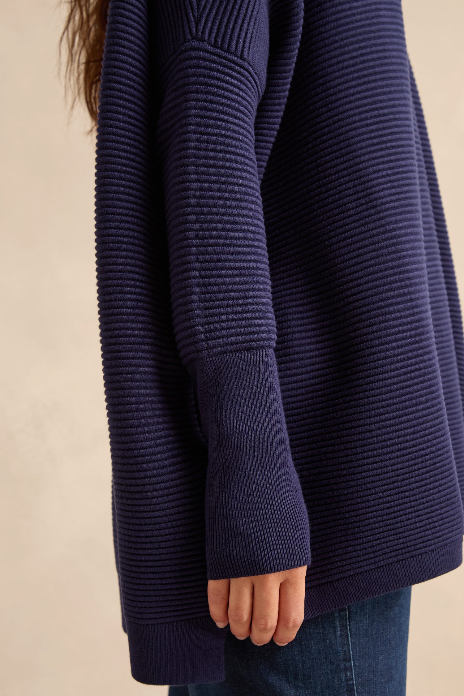 A person shown from the shoulder down is wearing the Navy Ribbed Jumper and dark jeans, with their arm relaxed at their side.
