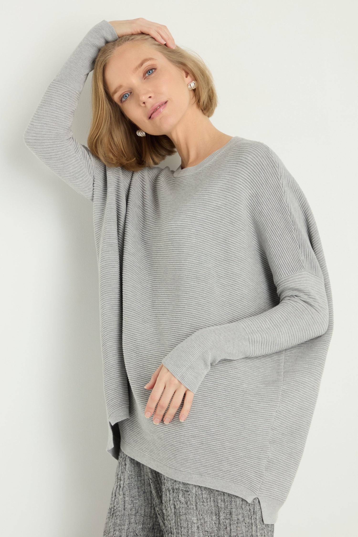 A woman with short blonde hair wears the Round Neck Ribbed Top in light gray with matching textured pants, standing against a plain light background.