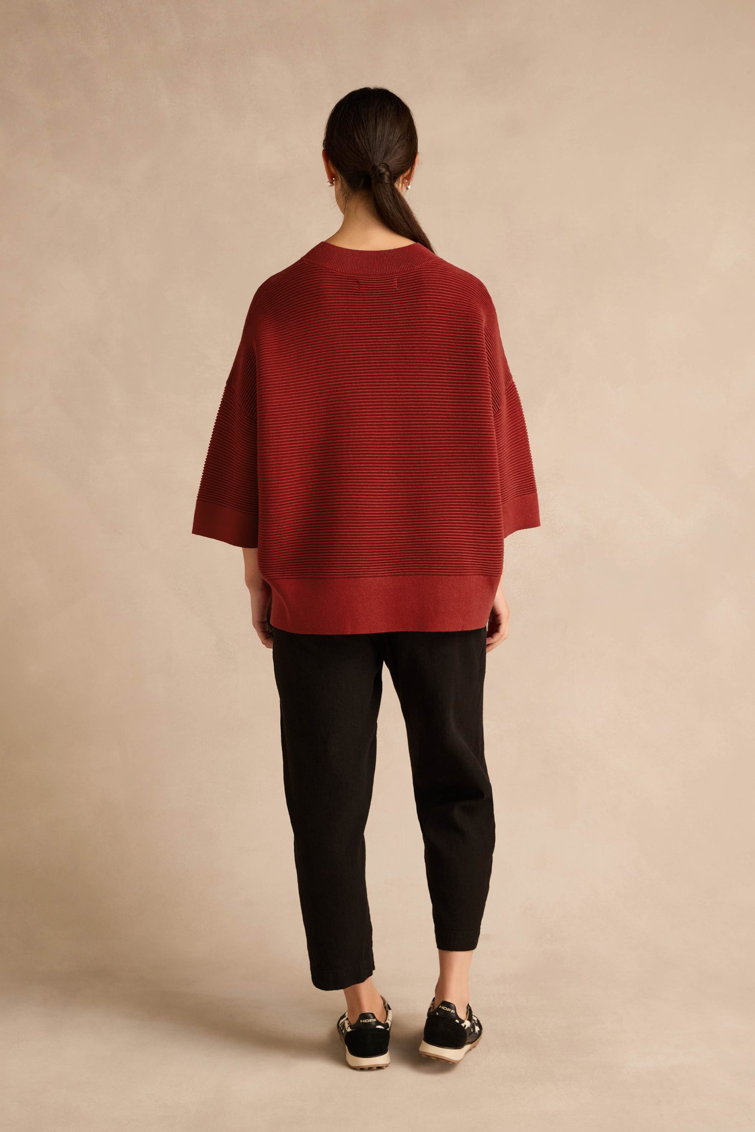 A person stands with their back to the camera, wearing the Wide Sleeve Burgundy Ribbed Knit sweater in a relaxed fit, paired with black cropped pants and black sneakers against a neutral background.