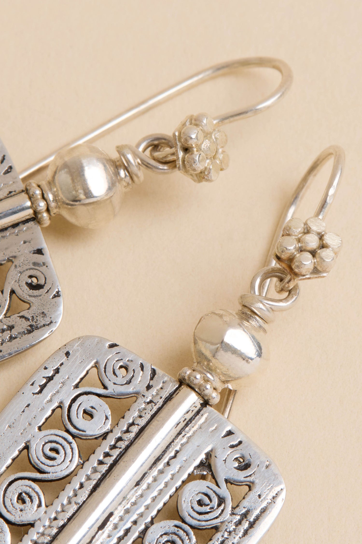 Close-up of Filigree Drop Earrings featuring ornate floral and swirl designs on a light beige background.