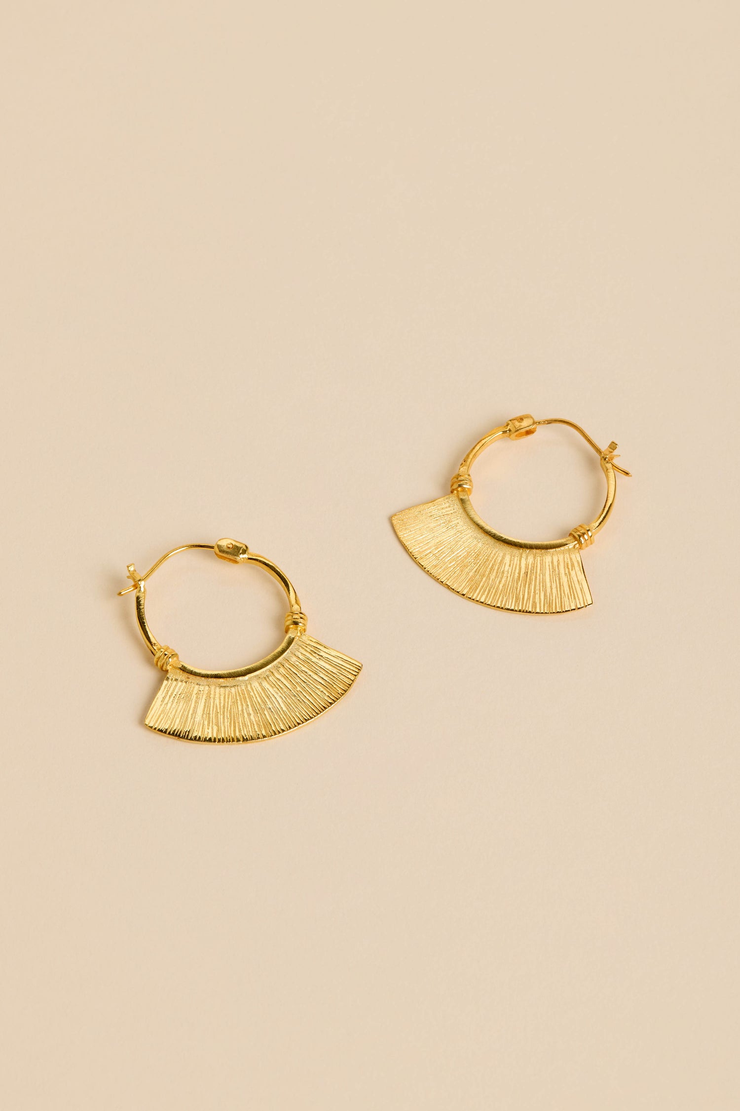 Gold-Plated Fan Hoop Earrings featuring textured, fan-shaped pendants are shown on a beige background.