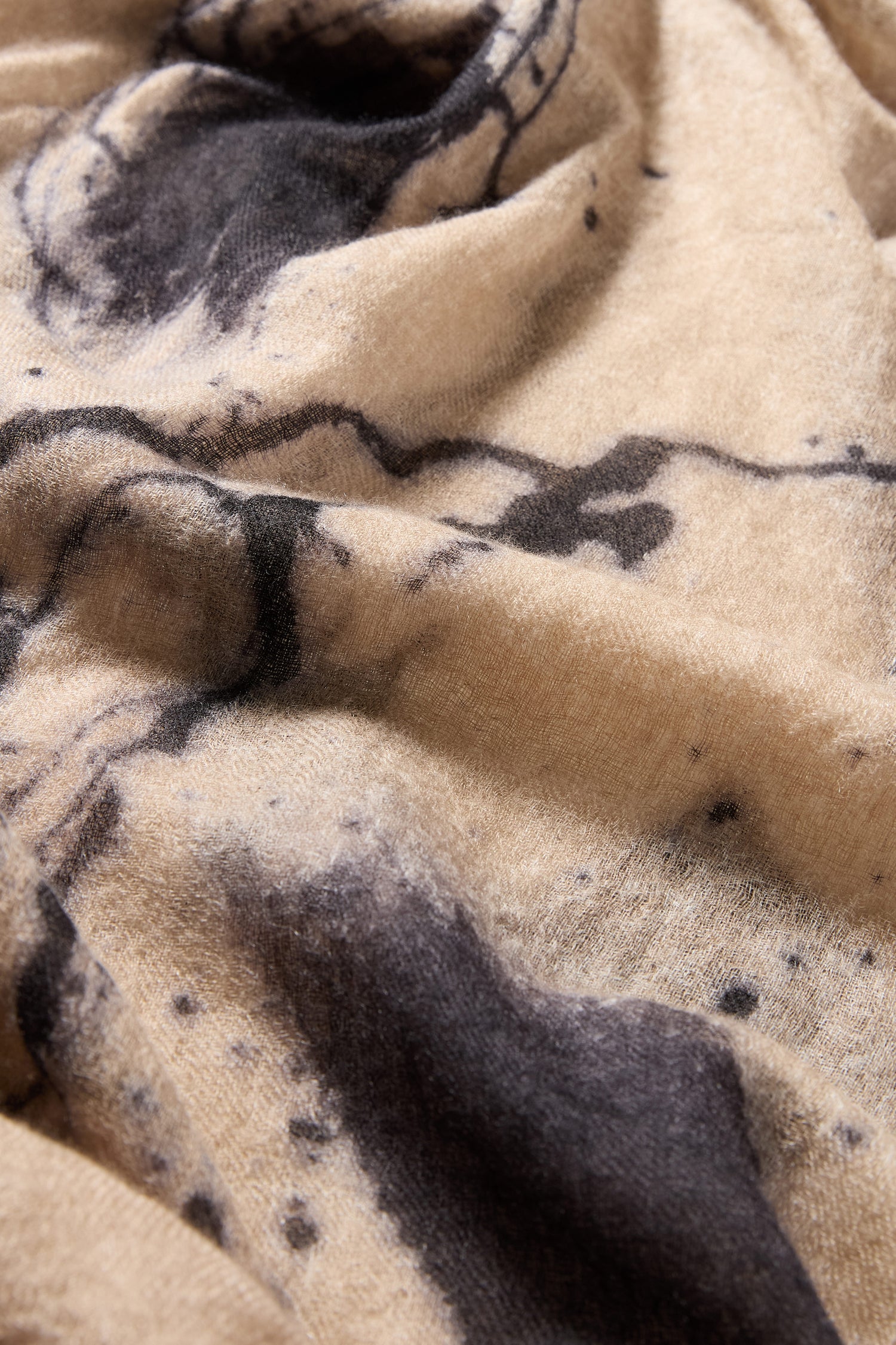 Close-up of the Painted Brushstroke Cashmere Scarf in beige, featuring irregular black brushstroke patterns and visible texture for a hand-painted look.