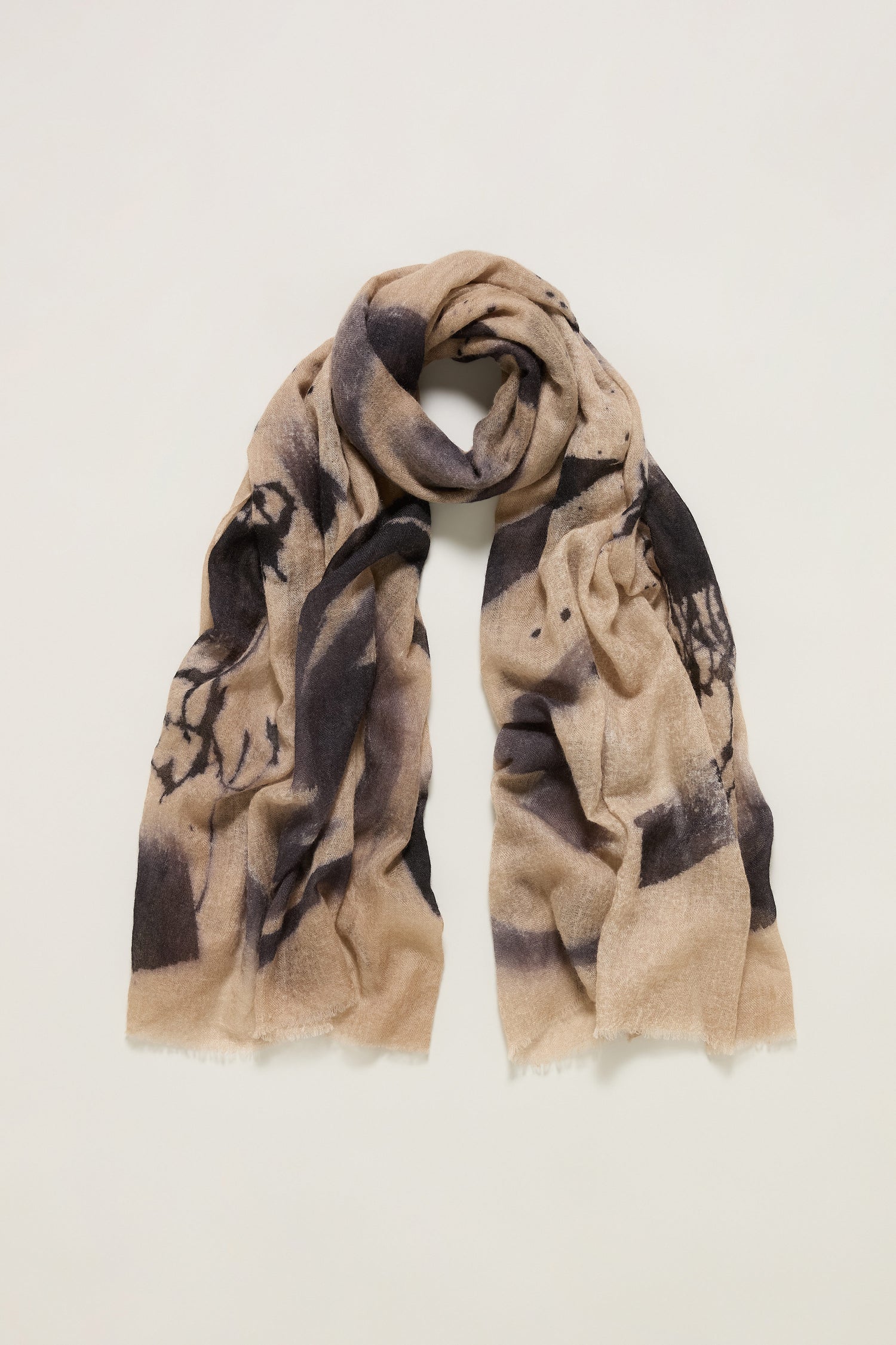 The Painted Brushstroke Cashmere Scarf features a beige base with a black brushstroke design, gently frayed edges, and is displayed flat on a light background.