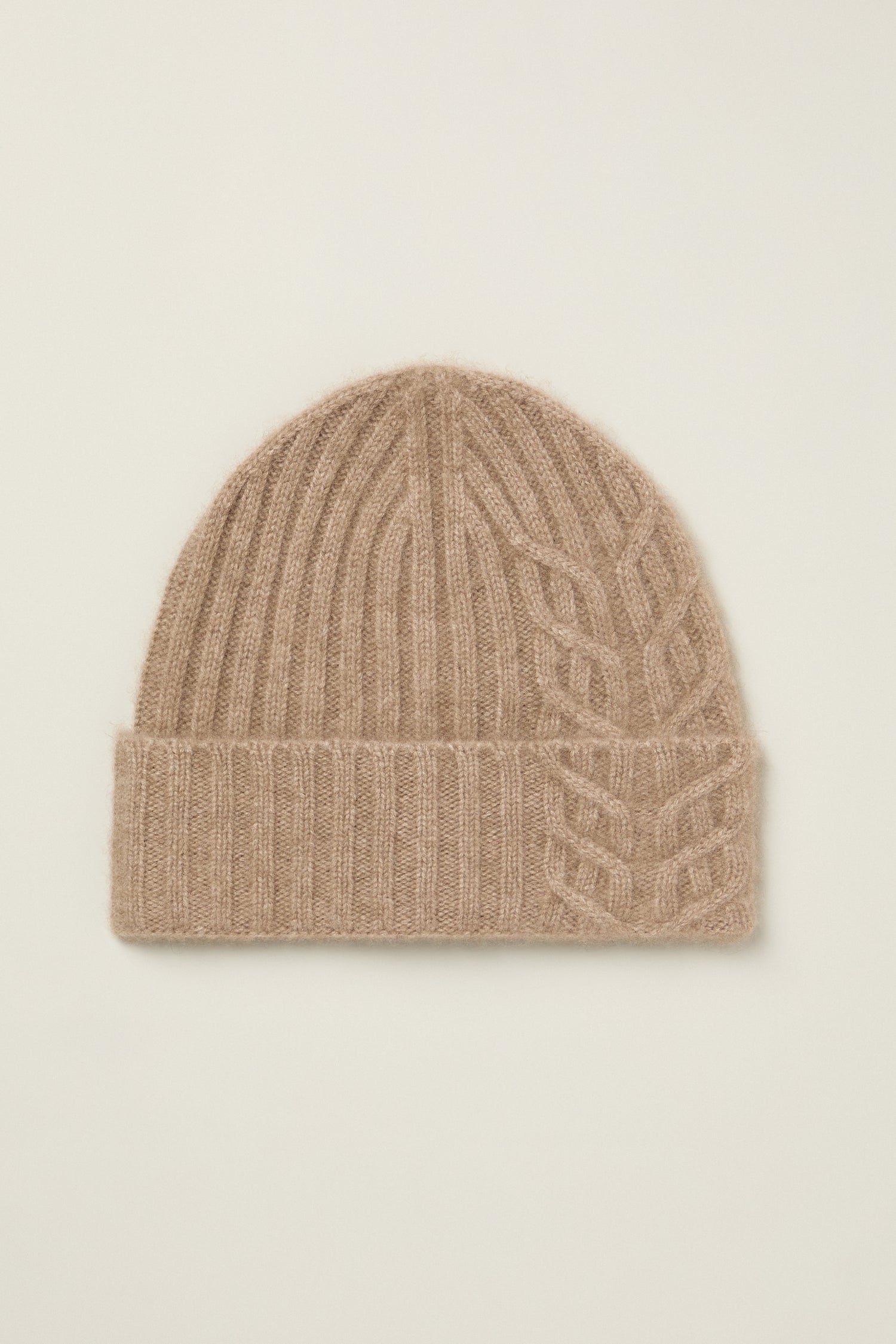 The Warm Sands Ribbed Cashmere Hat is a beige beanie featuring ribbed texture, a folded brim, and one-sided cable knit detail, shown against a plain background.