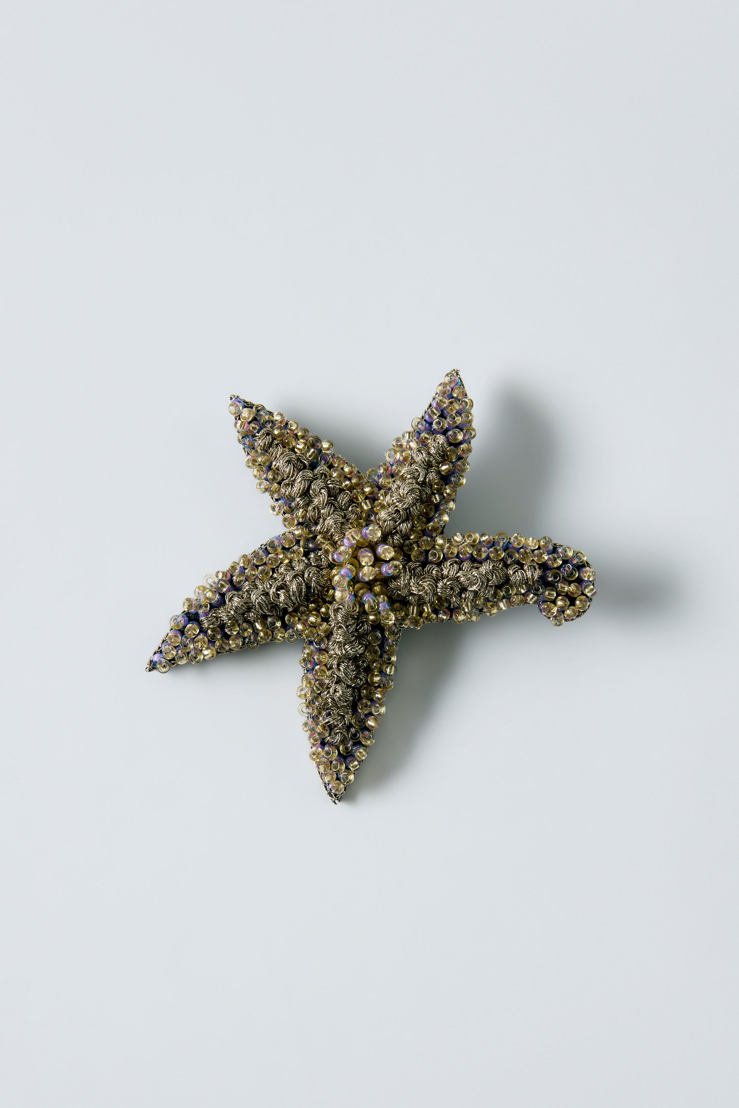 The Hand Beaded Starfish Brooch features decorative texture, crystal beads, and metallic accents, elegantly displayed on a plain light background.