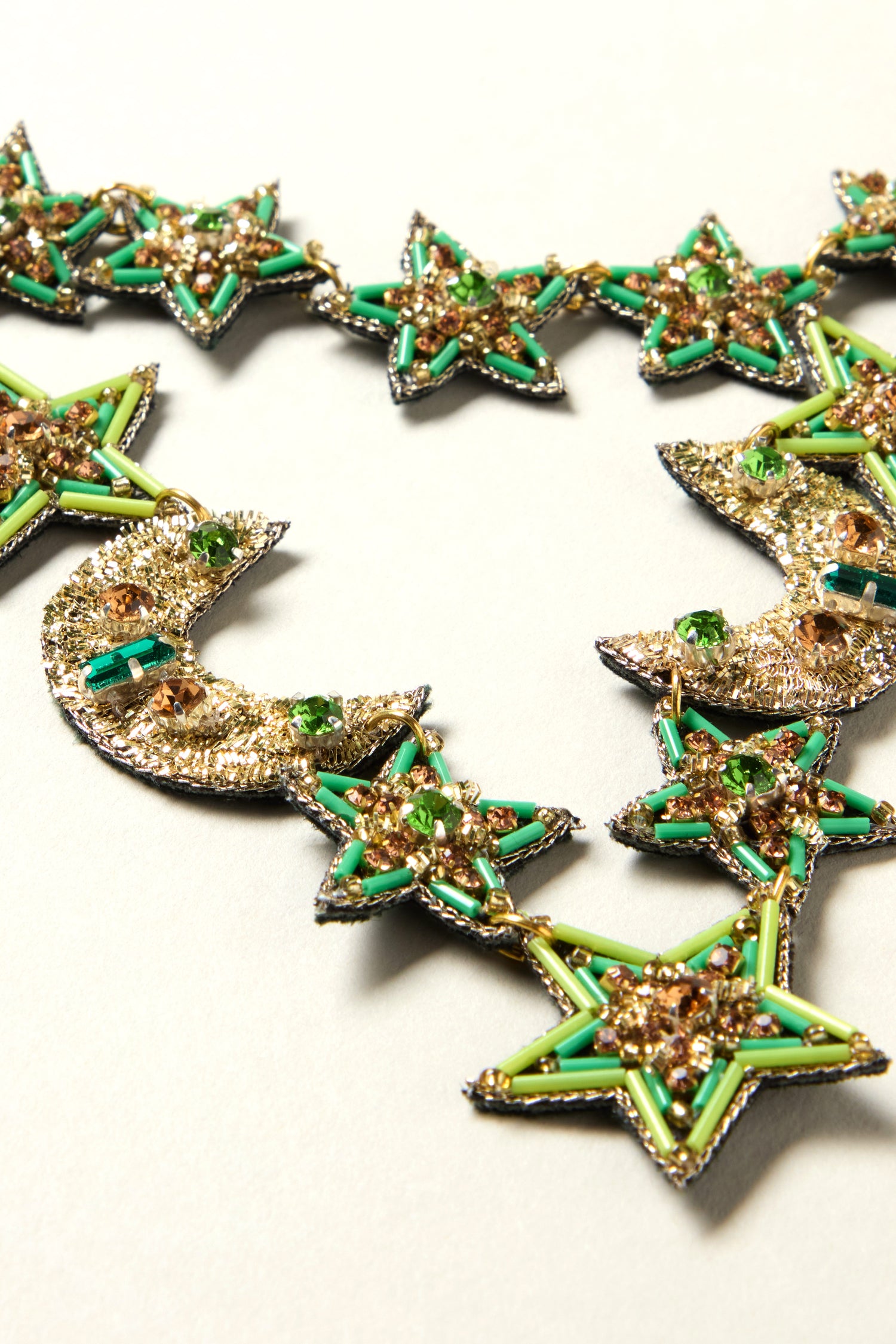 The Hand Beaded Celestial Necklace showcases handcrafted star and crescent moon beads in green, gold, and silver hues, artfully arranged for a striking and unique accessory.