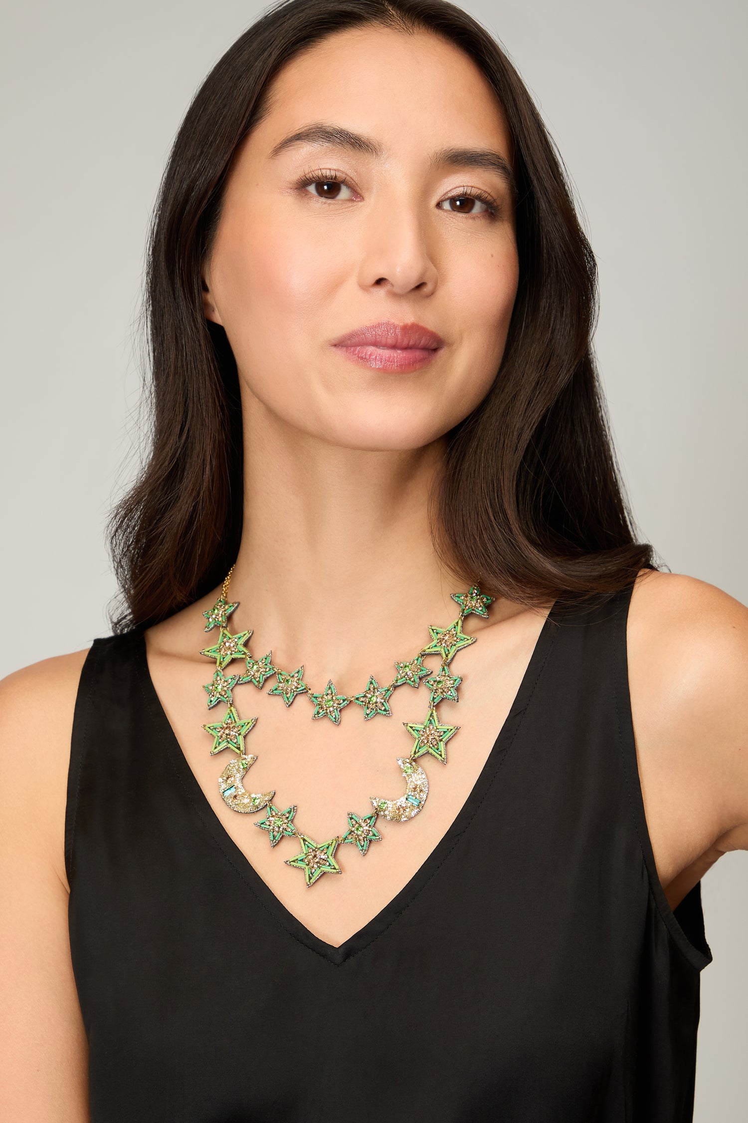 A woman with long dark hair wears a black sleeveless top and the Hand Beaded Celestial Necklace, a double-strand piece featuring green star and crescent moon beads—an exquisite example of handcrafted jewelry.