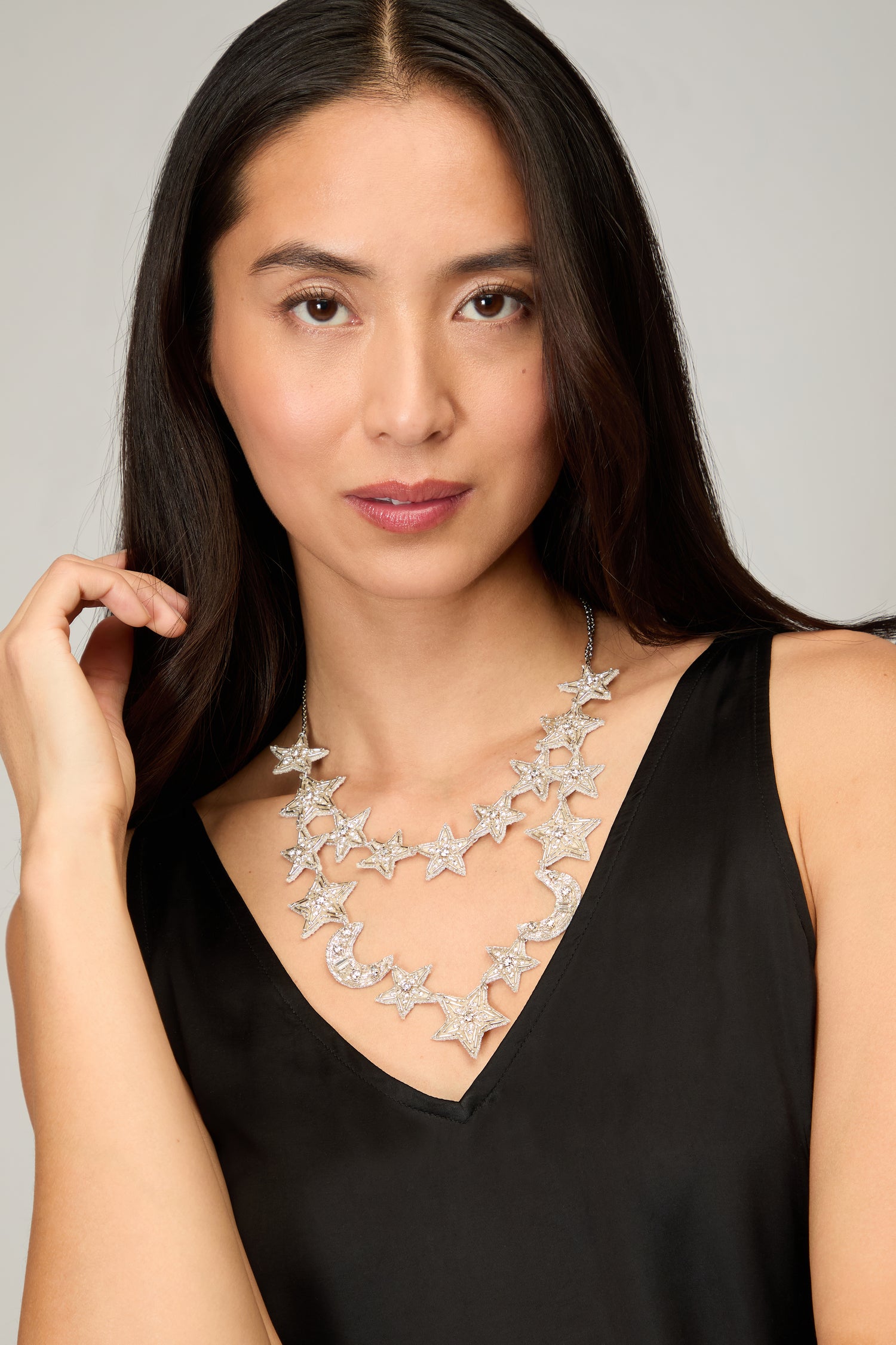 A woman with long dark hair wears a black sleeveless top and the Hand Beaded Celestial Necklace, a handcrafted statement piece adorned with silver stars and a crescent moon.