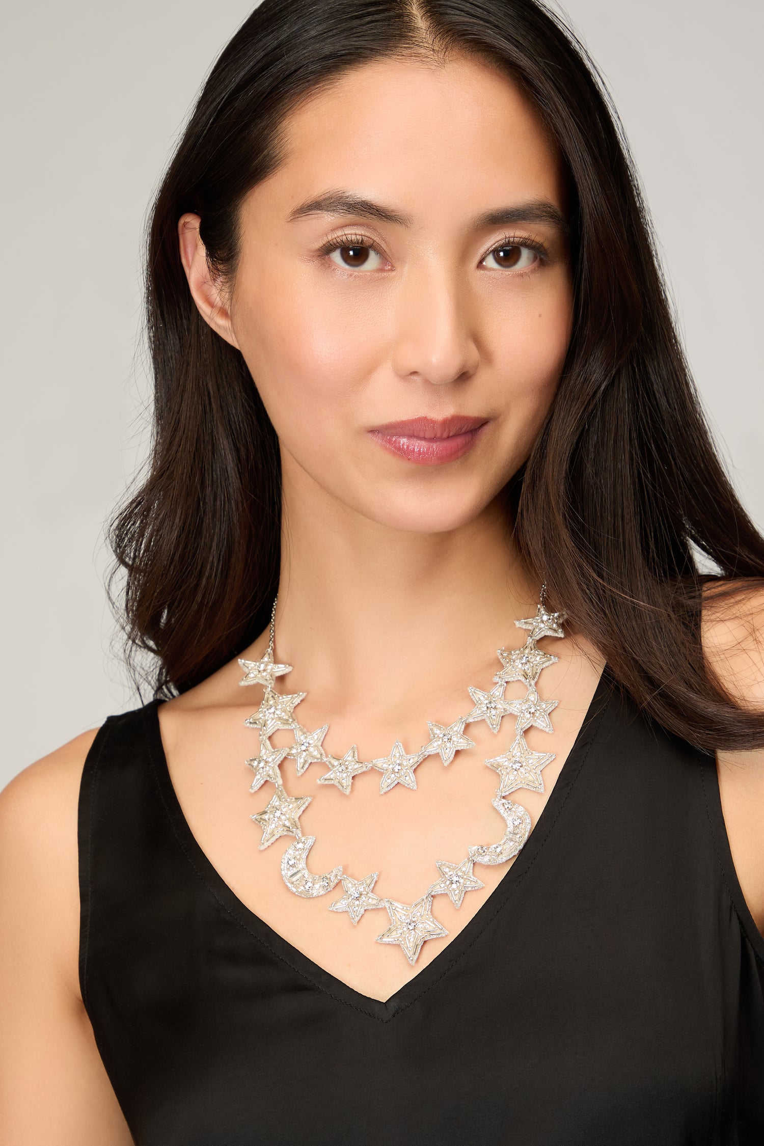 A woman in a sleeveless black top showcases the Hand Beaded Celestial Necklace—a handcrafted double-strand piece with layered silver star charms—against a neutral background.