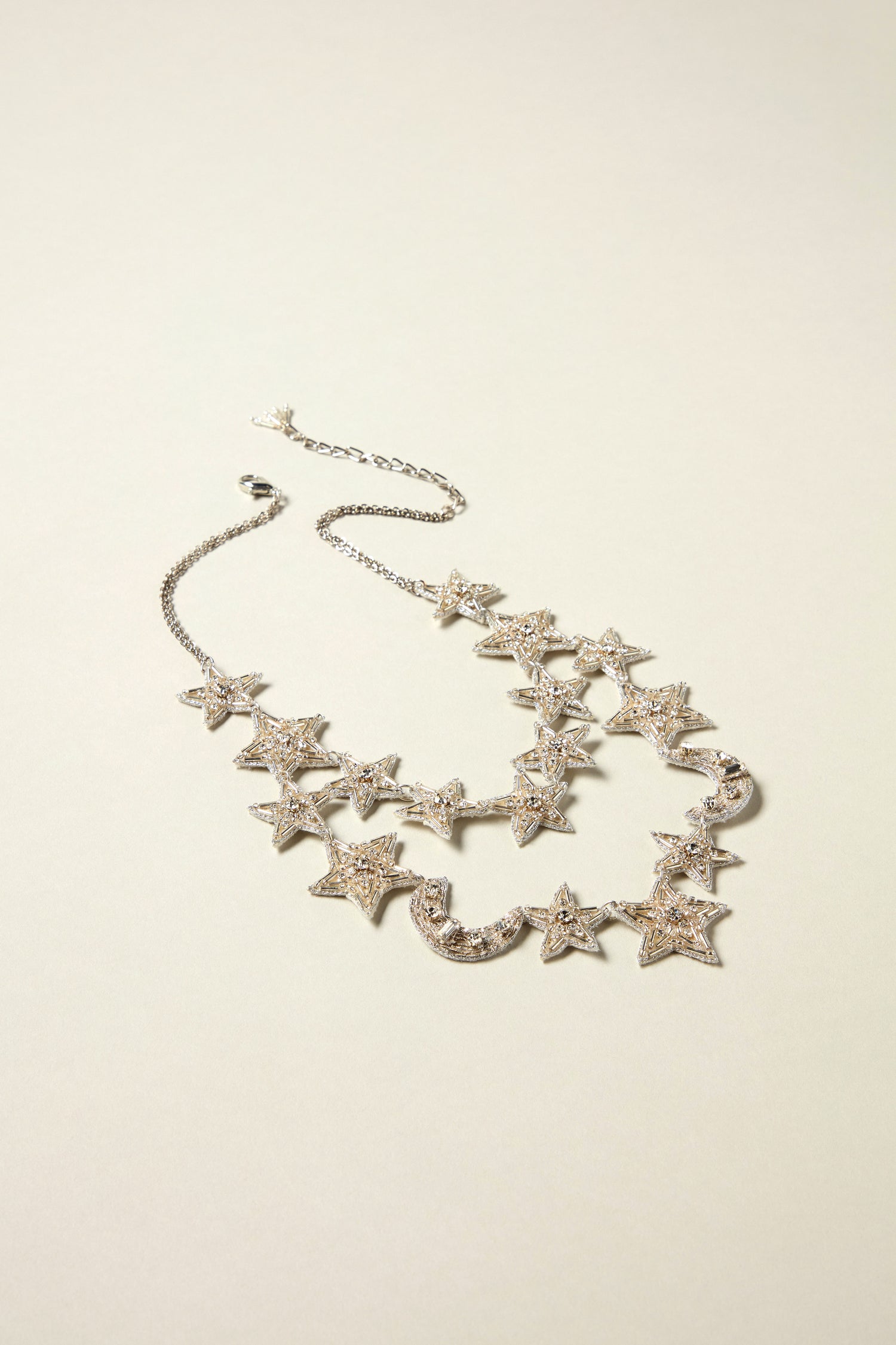 The Hand Beaded Celestial Necklace is a handcrafted silver double-strand piece featuring multiple star-shaped pendants with sparkly stones, beautifully presented on a plain light background.