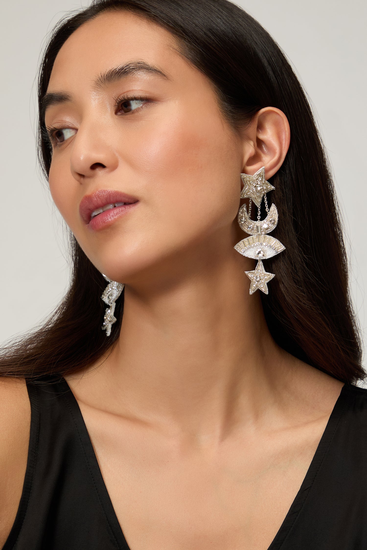 Woman with long dark hair wearing Psquuare Fashion Jewellery's Hand Beaded Celestial Silver Earrings, featuring star and crescent designs, paired with a sleeveless black top for a striking, modern look.