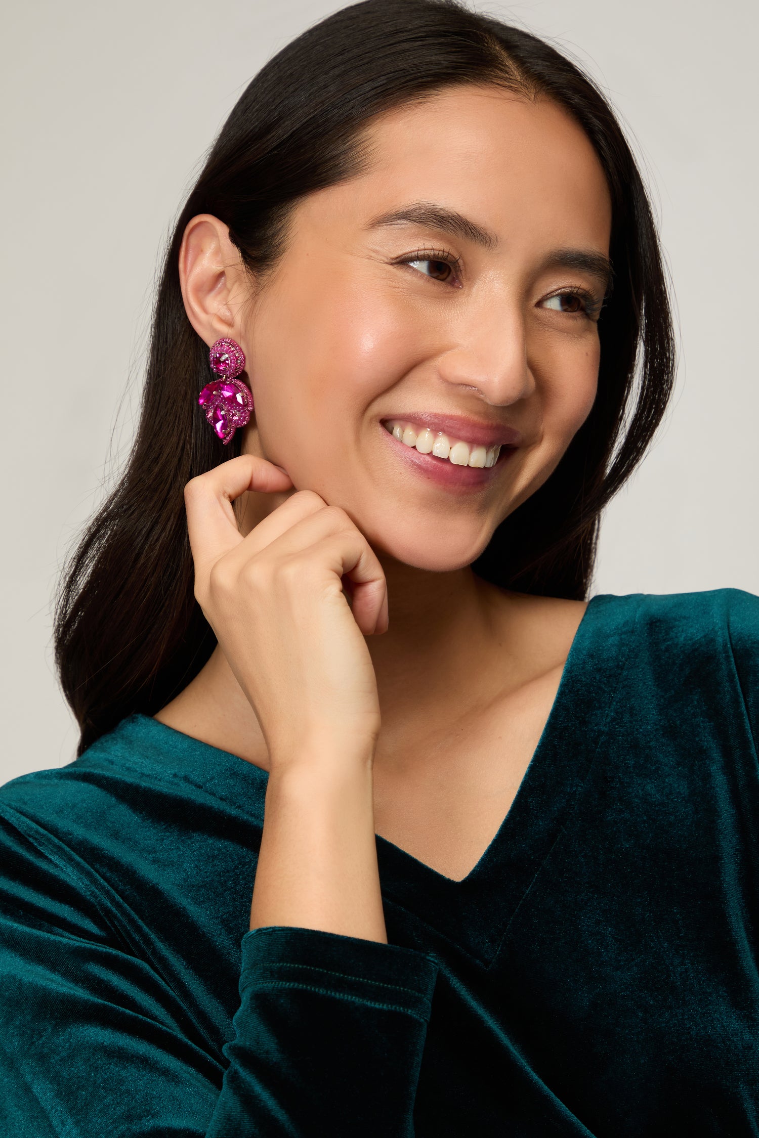 Woman with long dark hair smiles while touching her artisan Hand Beaded Flower Earrings, paired with a teal velvet top.