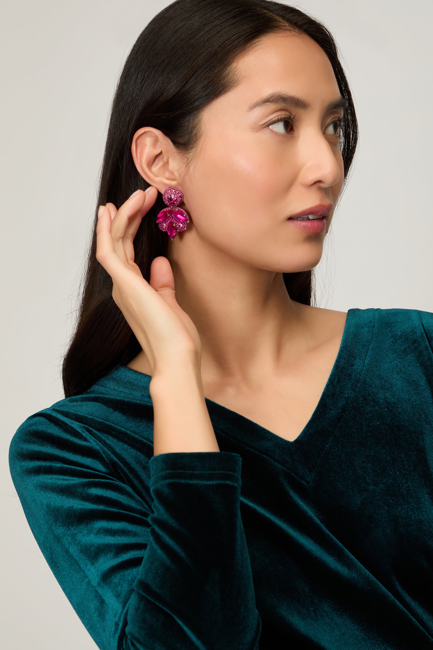 A woman in a teal velvet top holds her hand to her ear, showcasing Hand Beaded Flower Earrings—lightweight statement jewelry that adds a bold, artisan touch to her style.