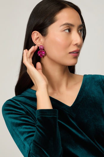 A woman in a teal velvet top holds her hand to her ear, showcasing Hand Beaded Flower Earrings—lightweight statement jewelry that adds a bold, artisan touch to her style.