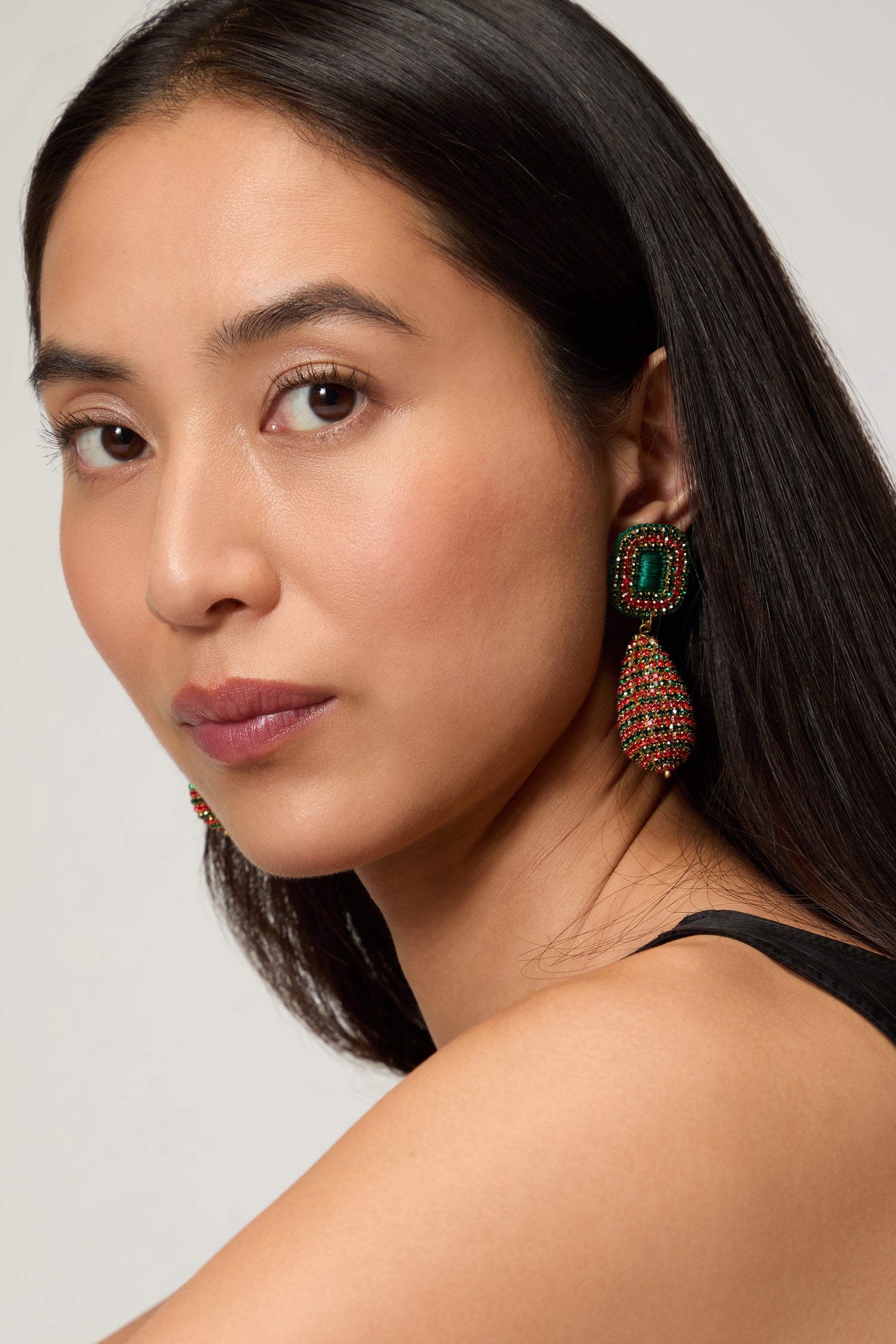 A woman with long dark hair wears a sleeveless black top and Hand Beaded Teardrop Earrings by Psquuare Fashion Jewellery, featuring emerald and red accents, as she looks at the camera against a neutral background.