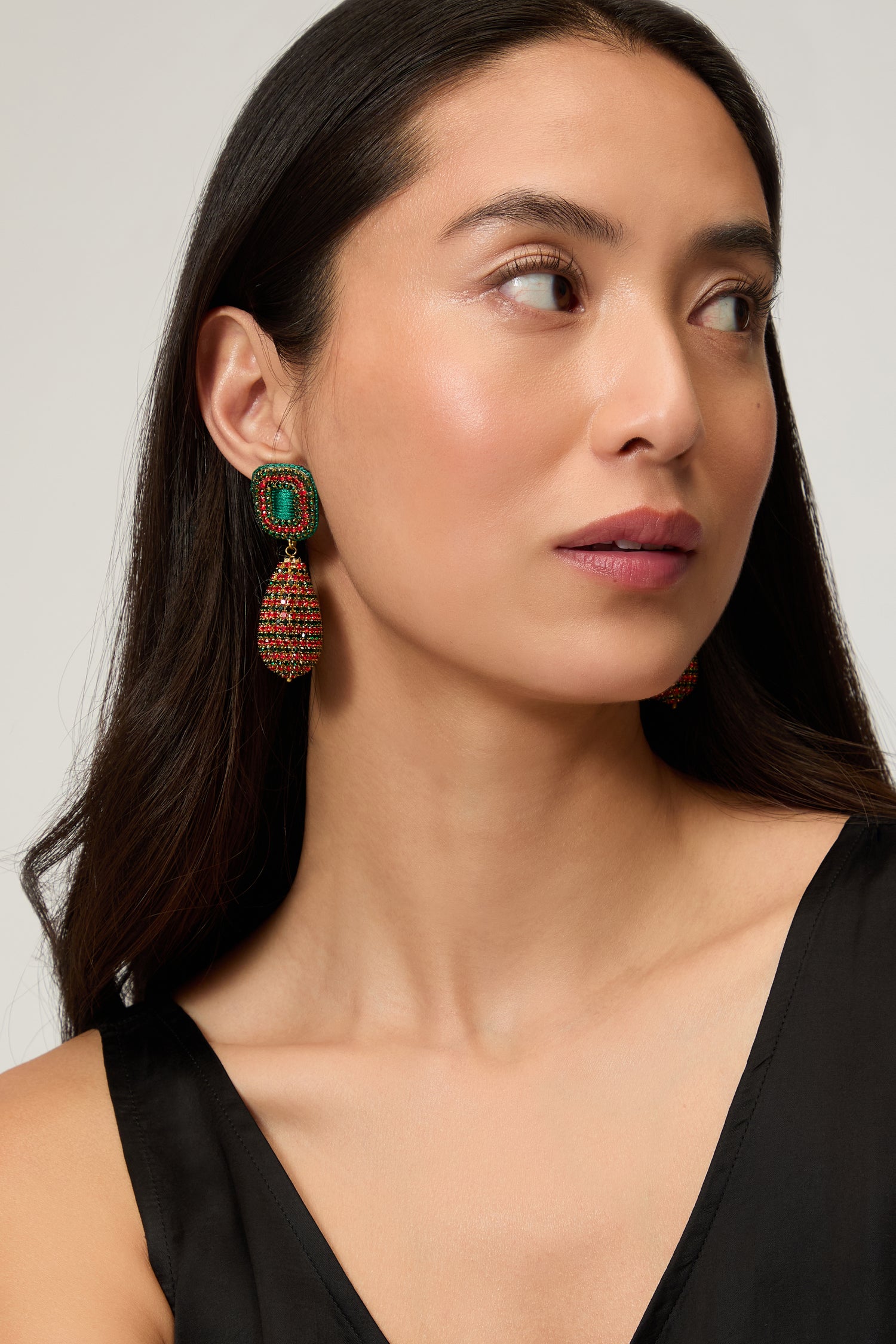 A woman with long dark hair, in a sleeveless black top, wears Hand Beaded Teardrop Earrings in green and brown, looking slightly to the side.