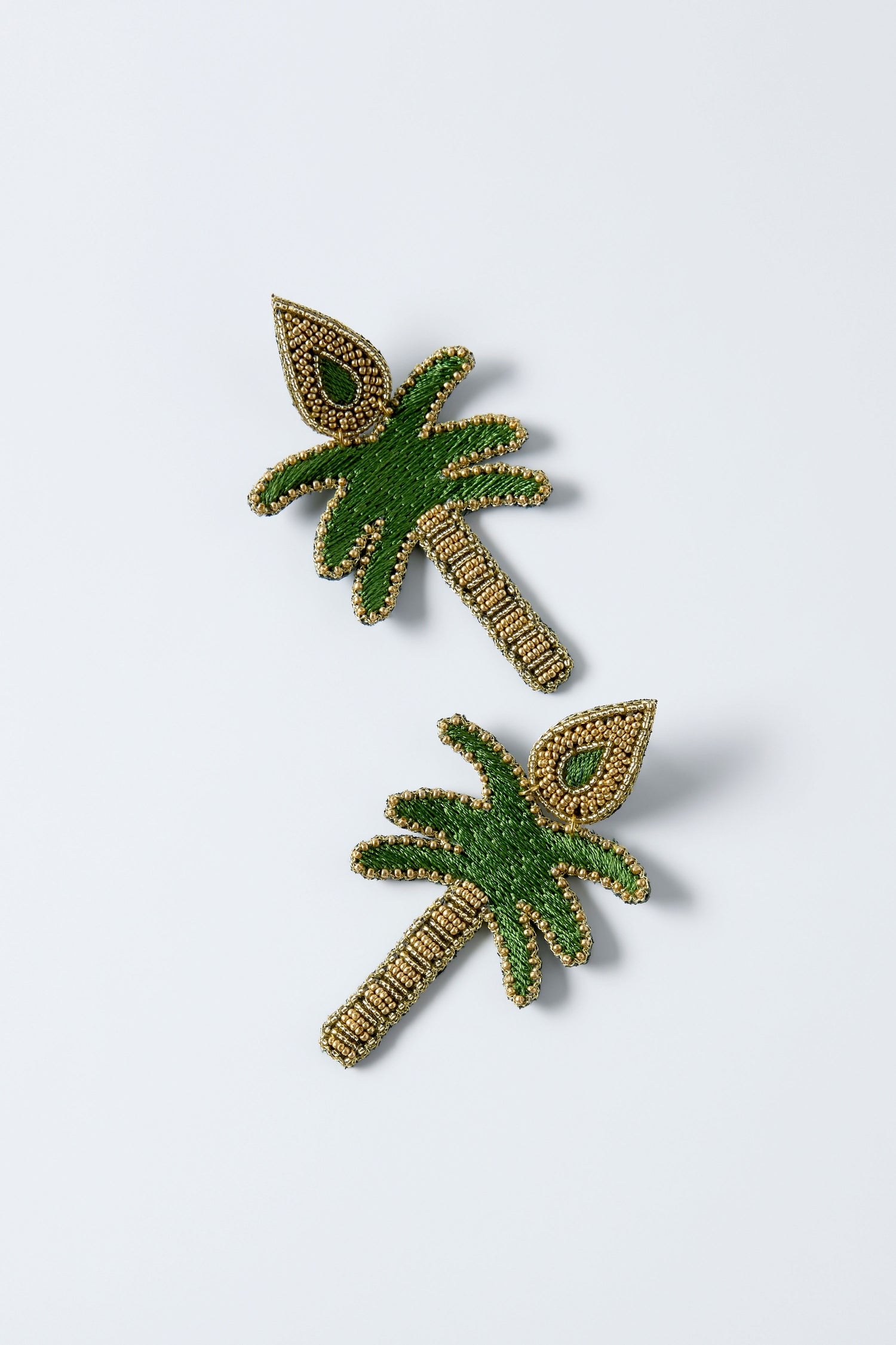 The Hand Embroidered Palm Earrings feature palm tree shapes with green and gold beadwork, resembling decorative pins, and are shown on a plain white background.