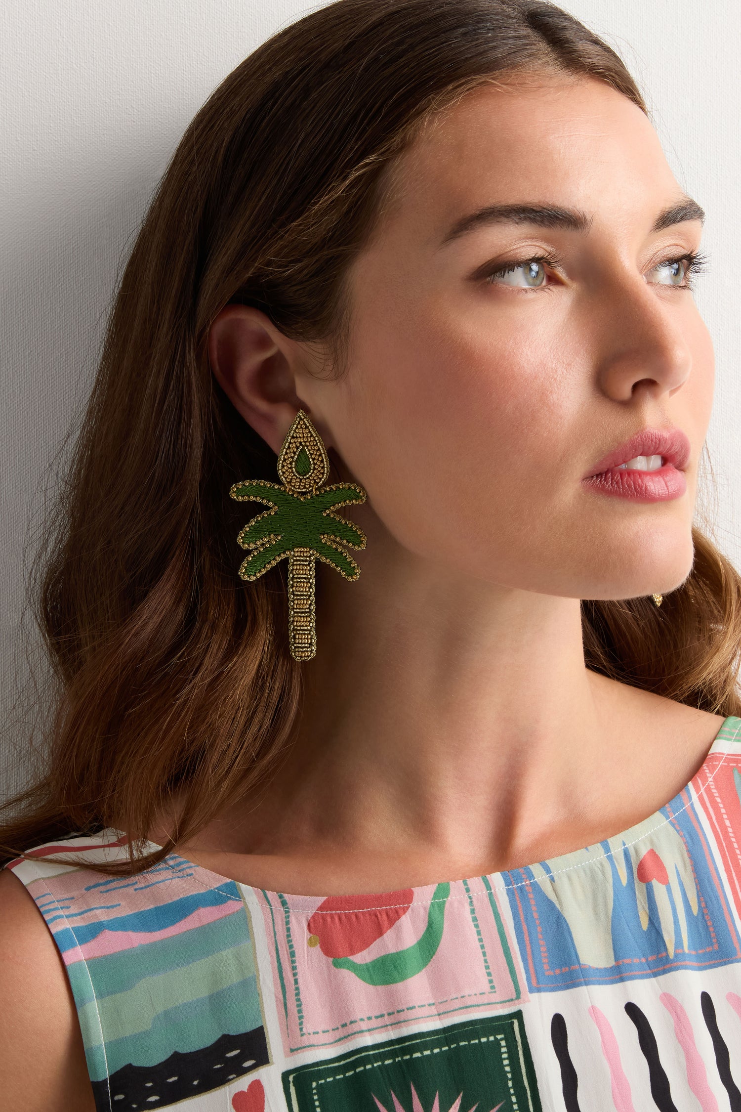 Woman with long brown hair wearing a sleeveless patterned dress and Hand Embroidered Palm Earrings, looking slightly to the side.