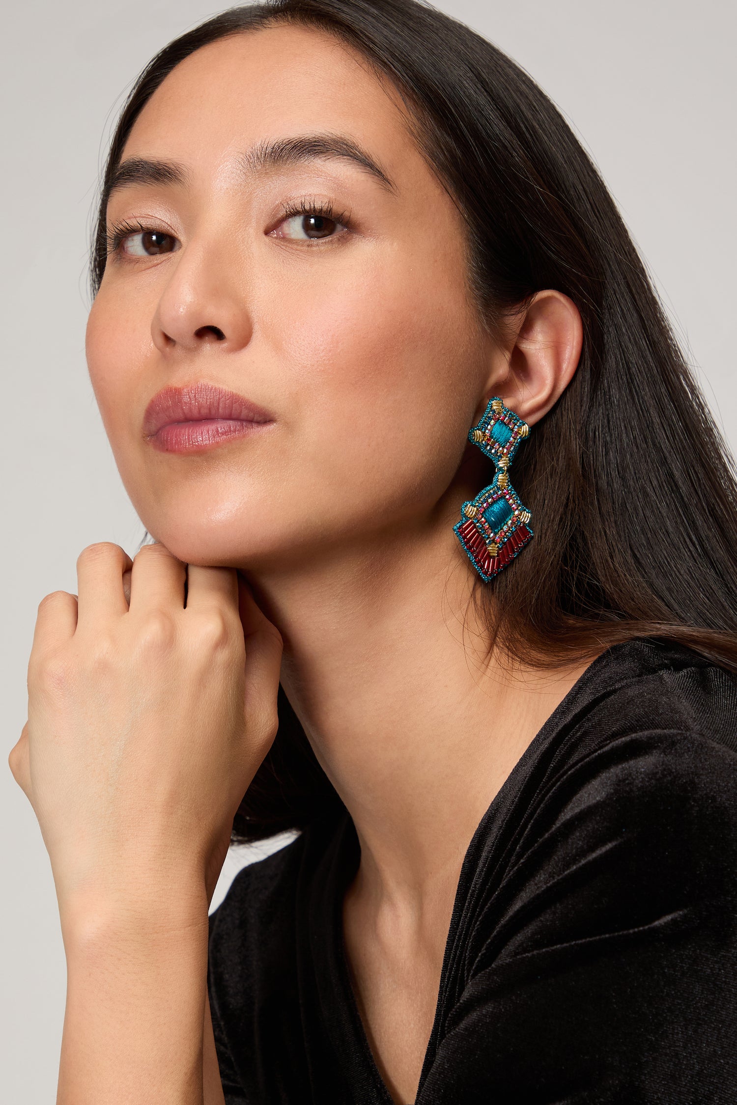 A woman with long dark hair and a black top rests her chin on her hand, showcasing the Hand Embroidered Square Drop Earrings against a plain background.
