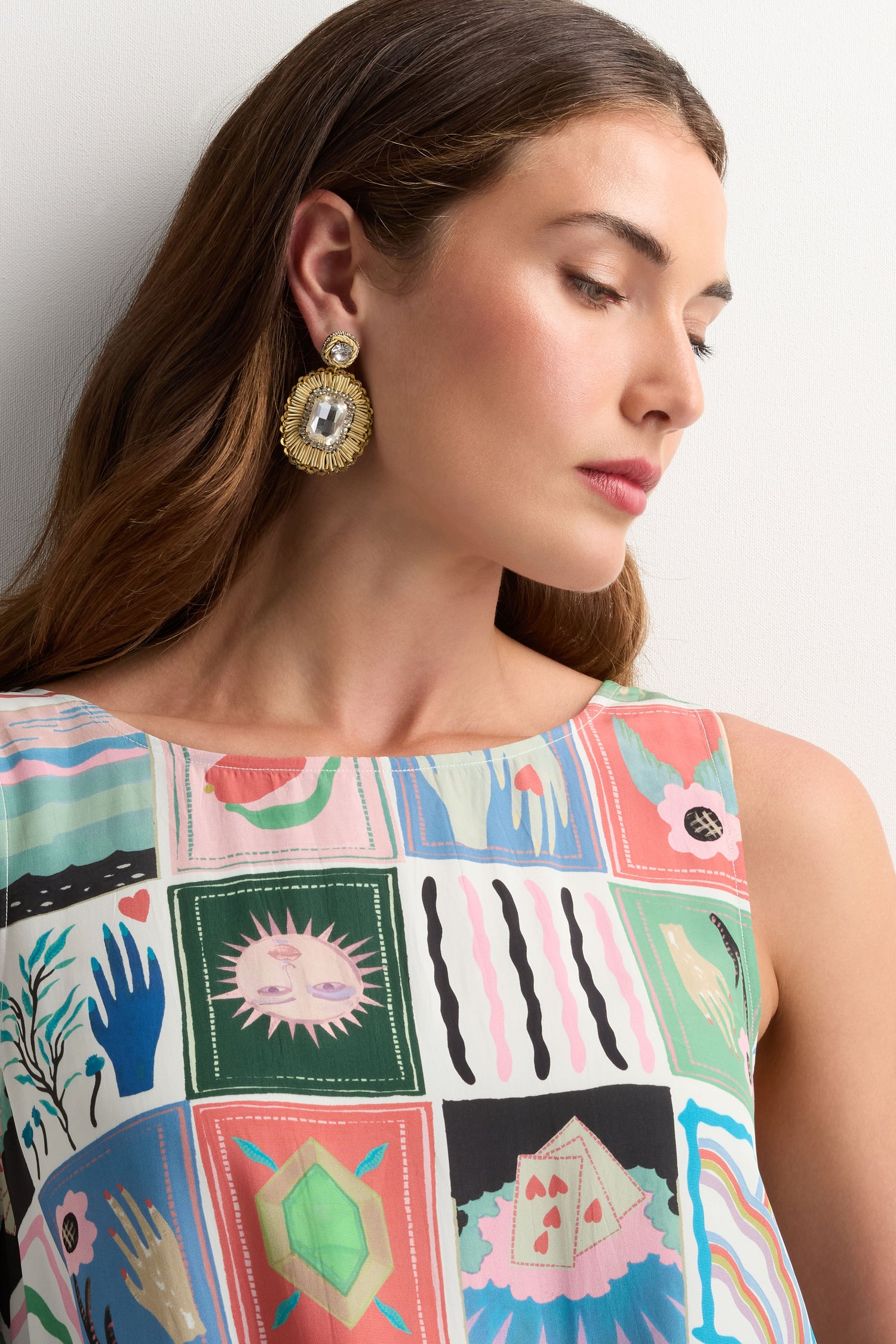 Woman with long brown hair wears a colorful sleeveless top and Hand Embroidered Ornate Earrings, accented with crystals, looking down and away from the camera.