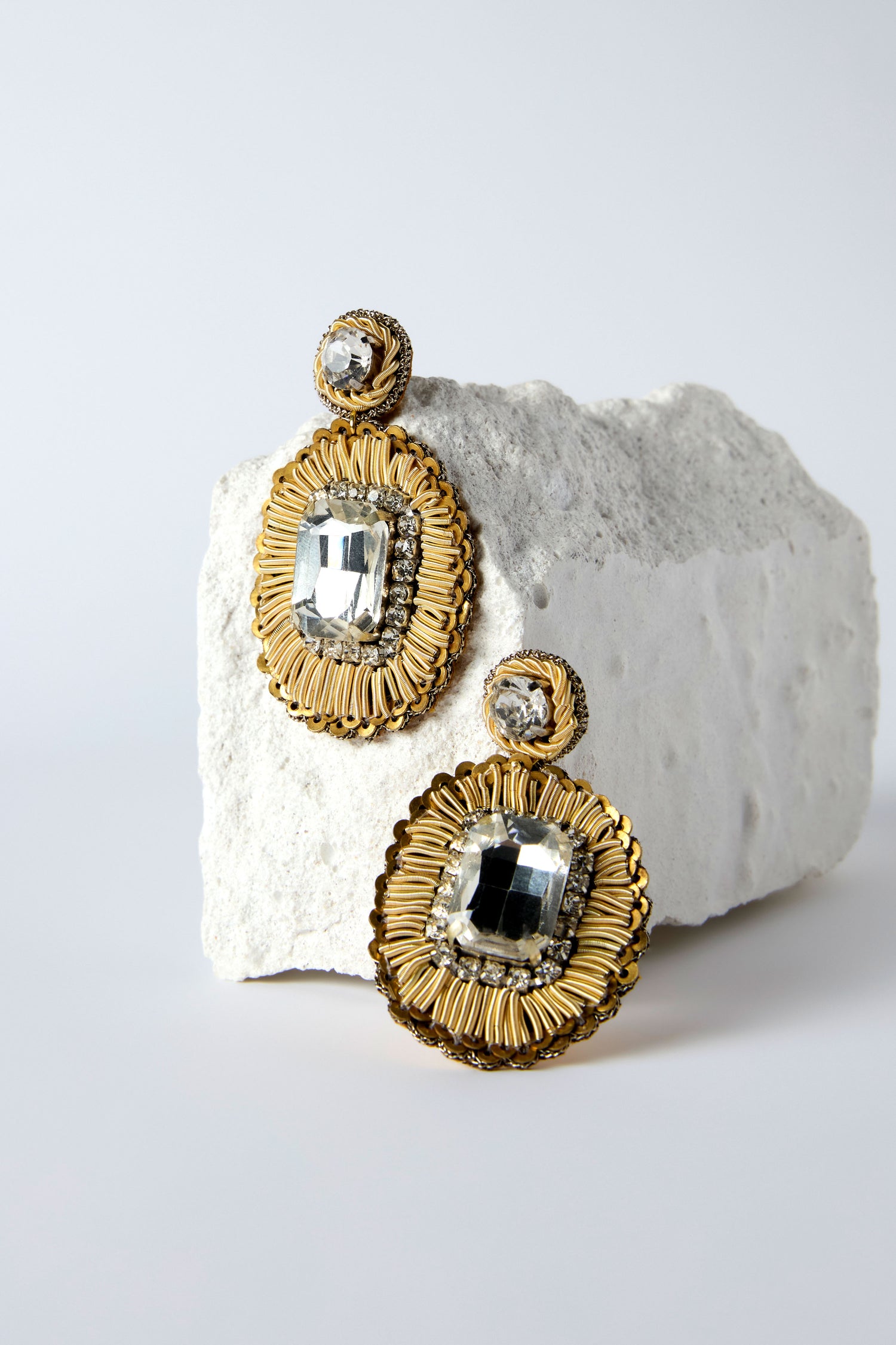 Hand Embroidered Ornate Earrings with gold and crystal beads are shown against a rough white stone background, featuring delicate hand-beaded studs for an elegant look.