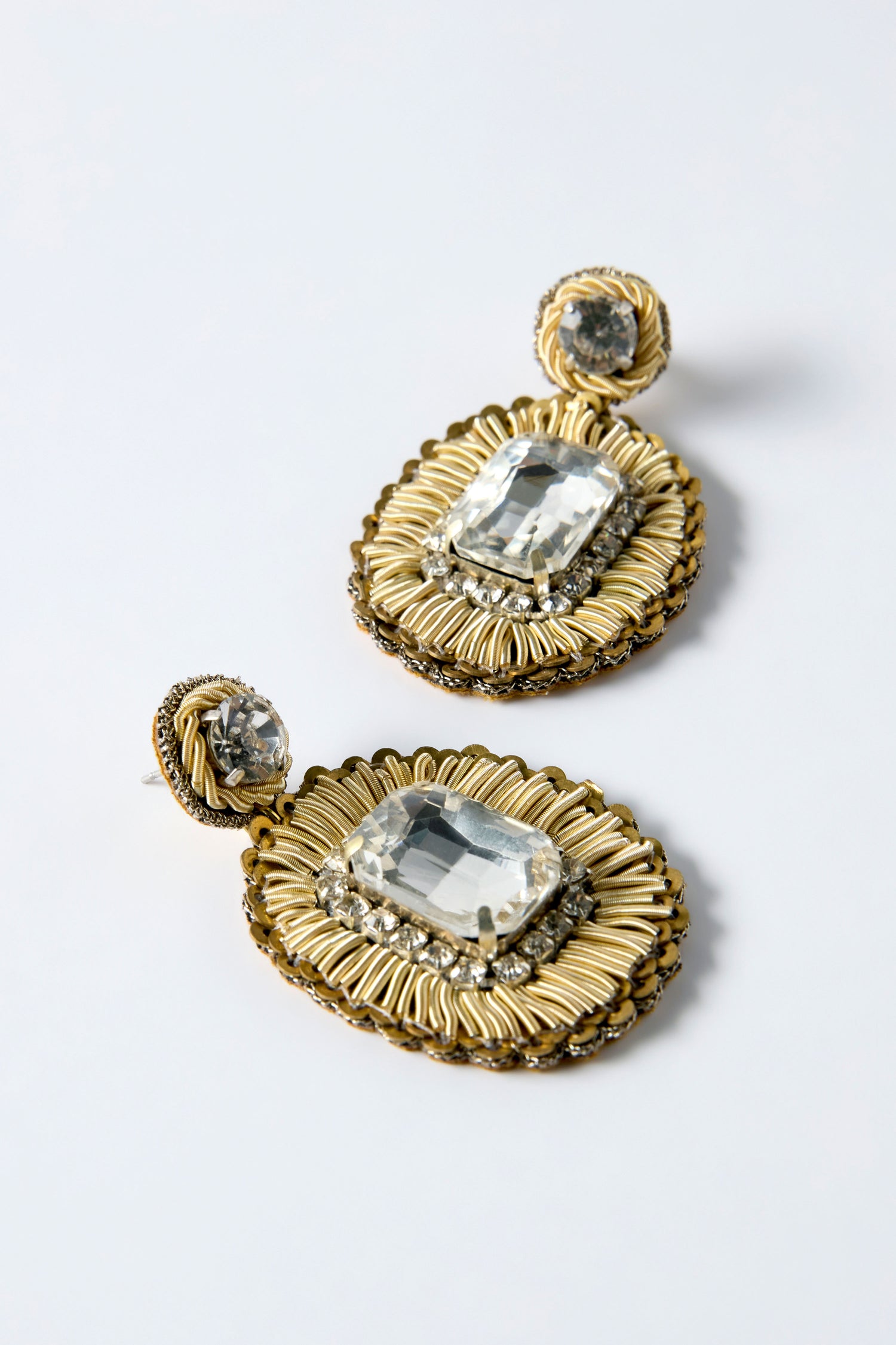 Hand Embroidered Ornate Earrings featuring gold textured brass, intricate designs, and large rectangular clear gemstones set in the center, displayed on a light background.
