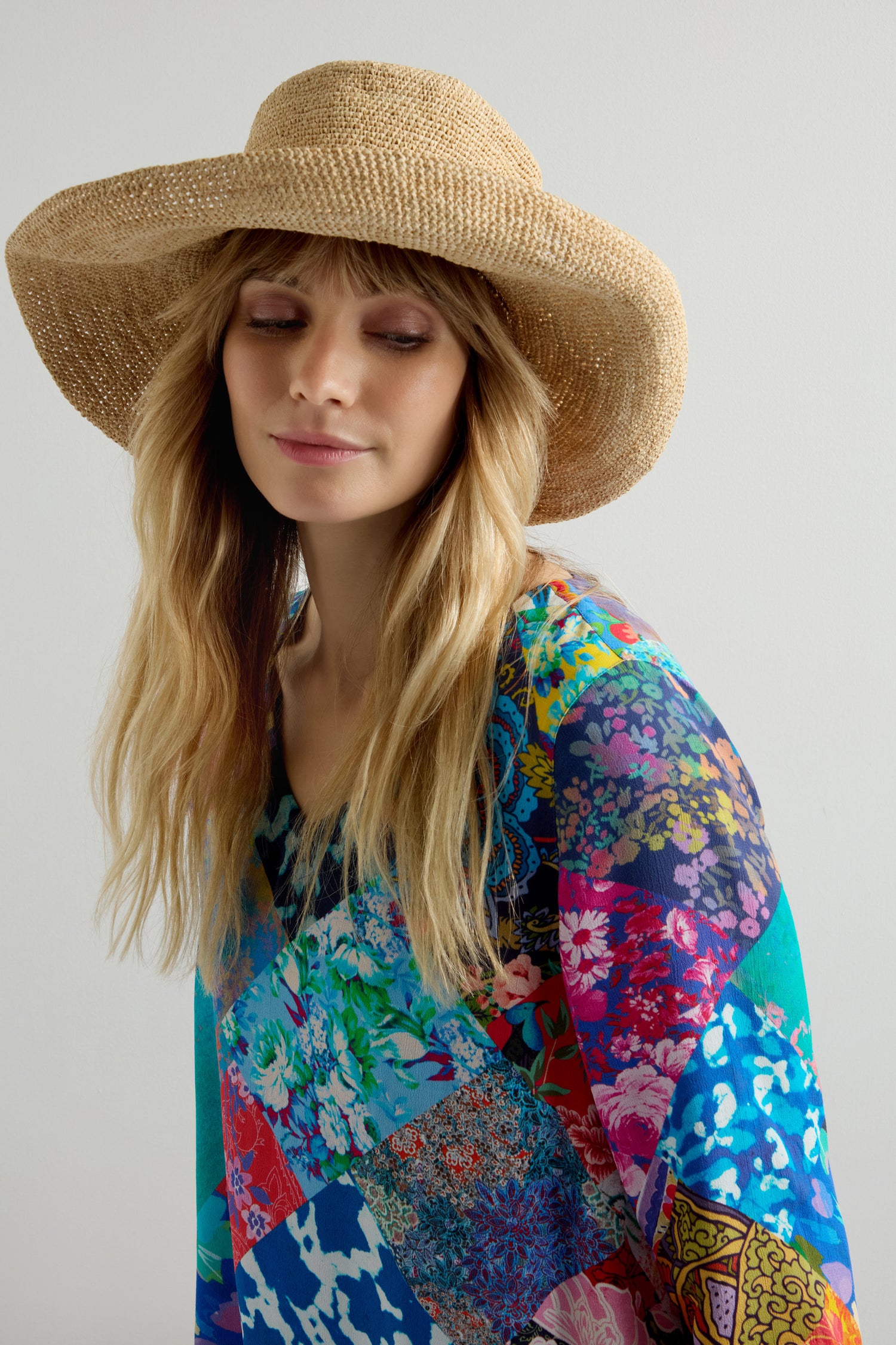 Person wearing a Handwoven Wide Brim Raffia Hat and a colorful floral-patterned blouse, looking down with a neutral expression.