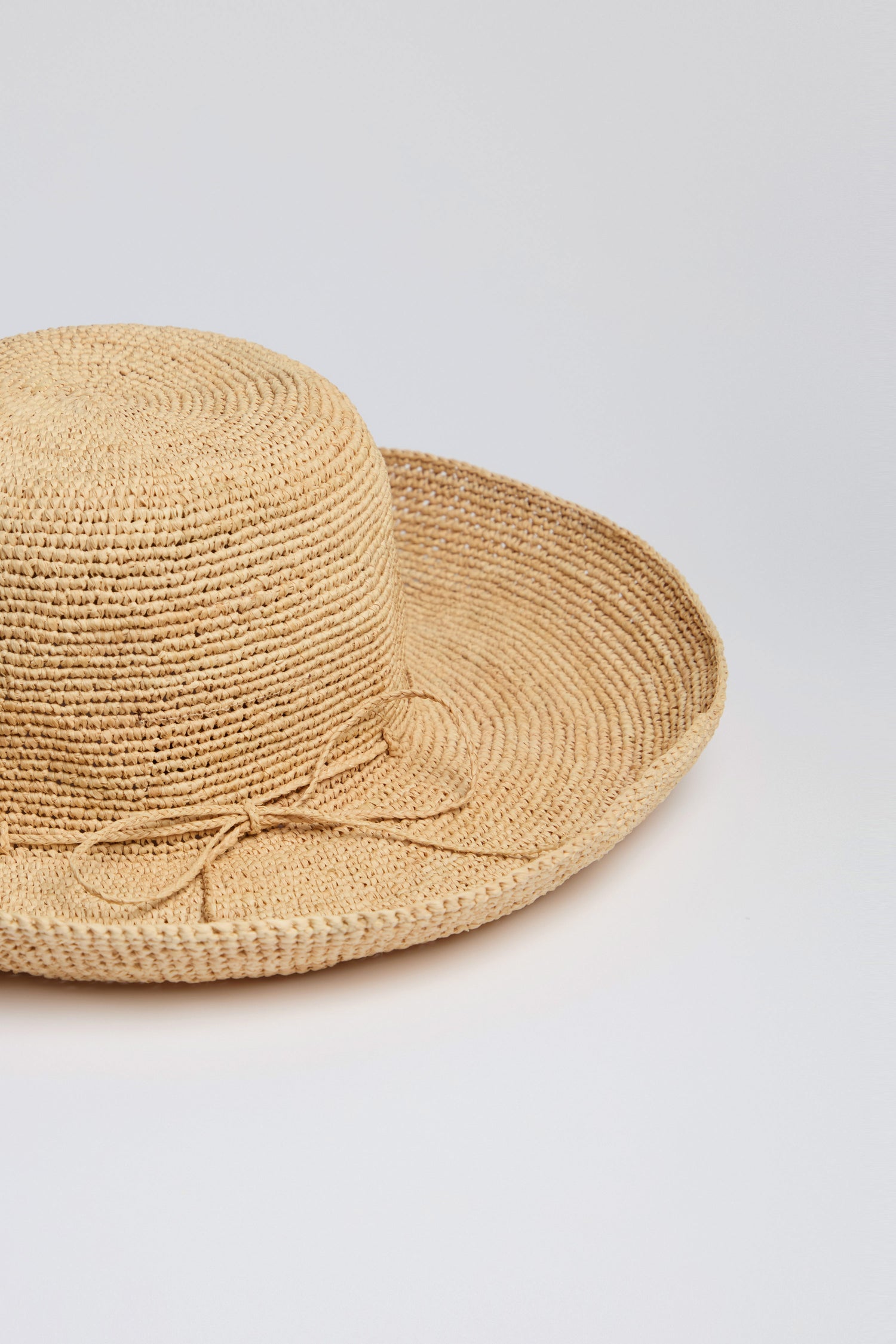 The Handwoven Wide Brim Raffia Hat features a round brim and decorative side bow, providing excellent sun protection against a plain white background.