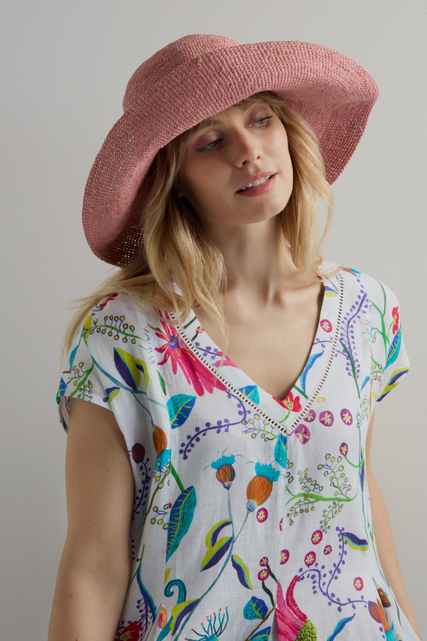 A person models the Handwoven Wide Brim Raffia Hat and a white floral-patterned top, standing against a neutral background and seamlessly blending style with sun protection.