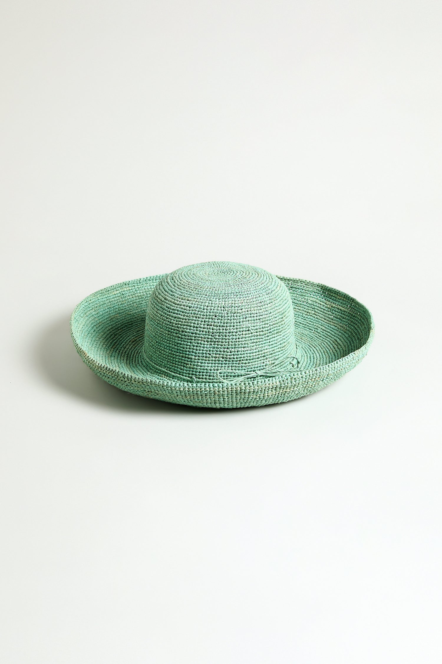 The Handwoven Wide Brim Raffia Hat, showcased against a plain white background, features mint green raffia crafted in Madagascar.
