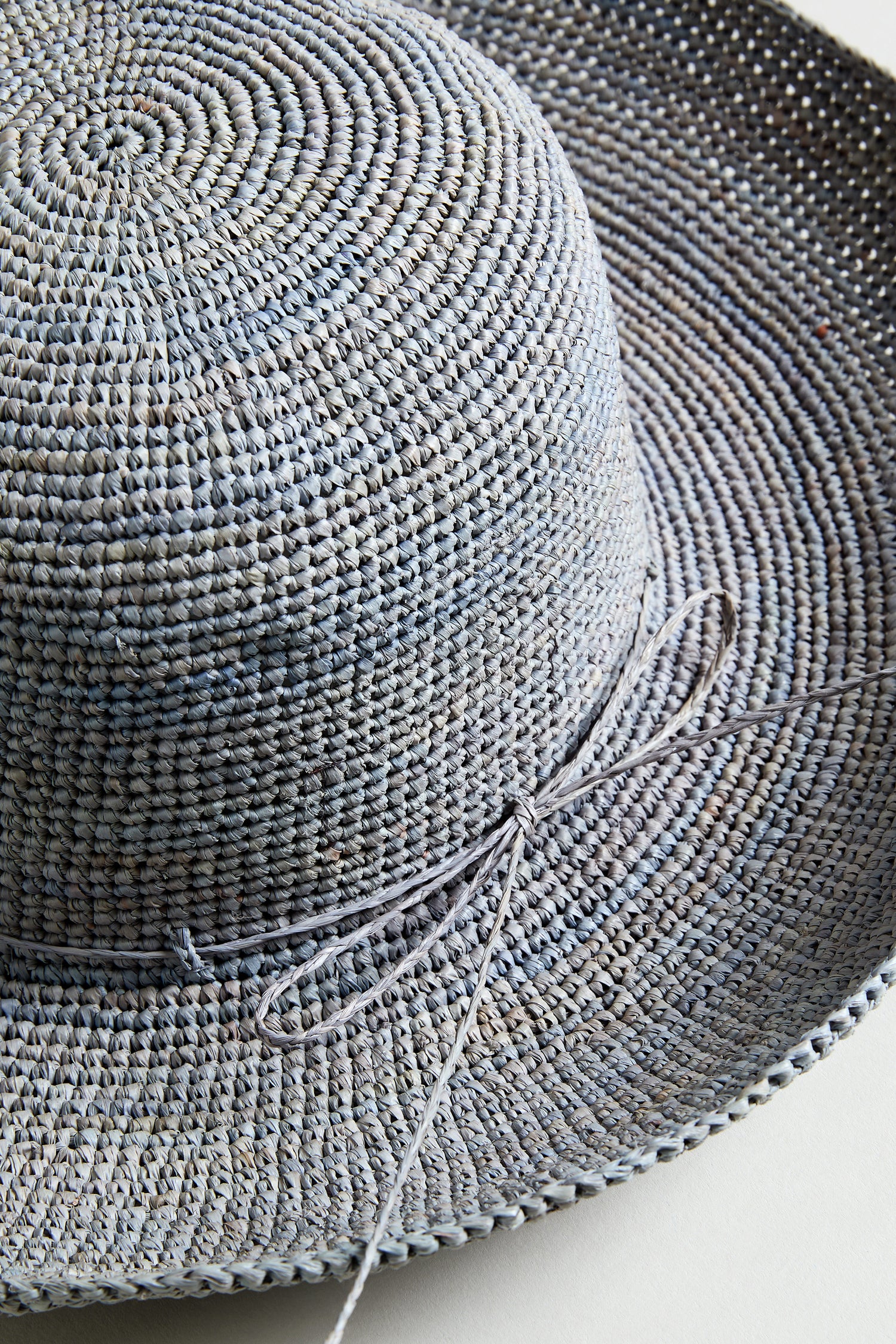 Close-up of the Handwoven Wide Brim Raffia Hat, crafted in Madagascar with a round crown, wide brim, and tied string bow detail.