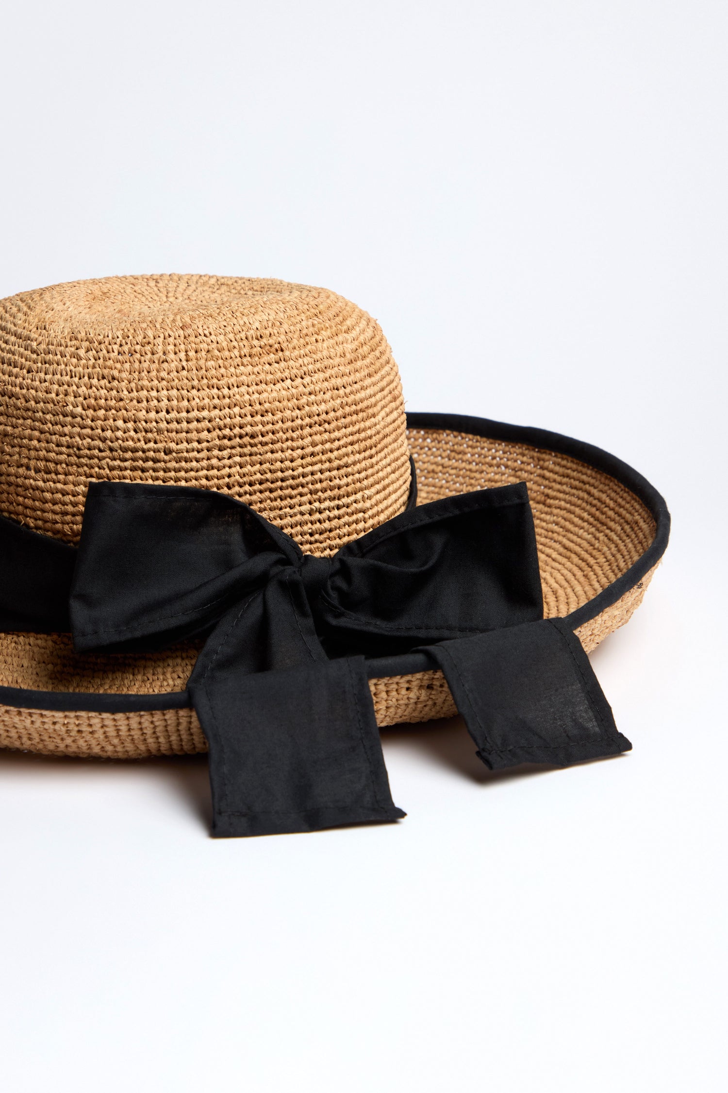 Enhance your summer style with the Handwoven Ribbon Raffia Hat, featuring a wide brim and adorned with a large black ribbon tied in a bow.