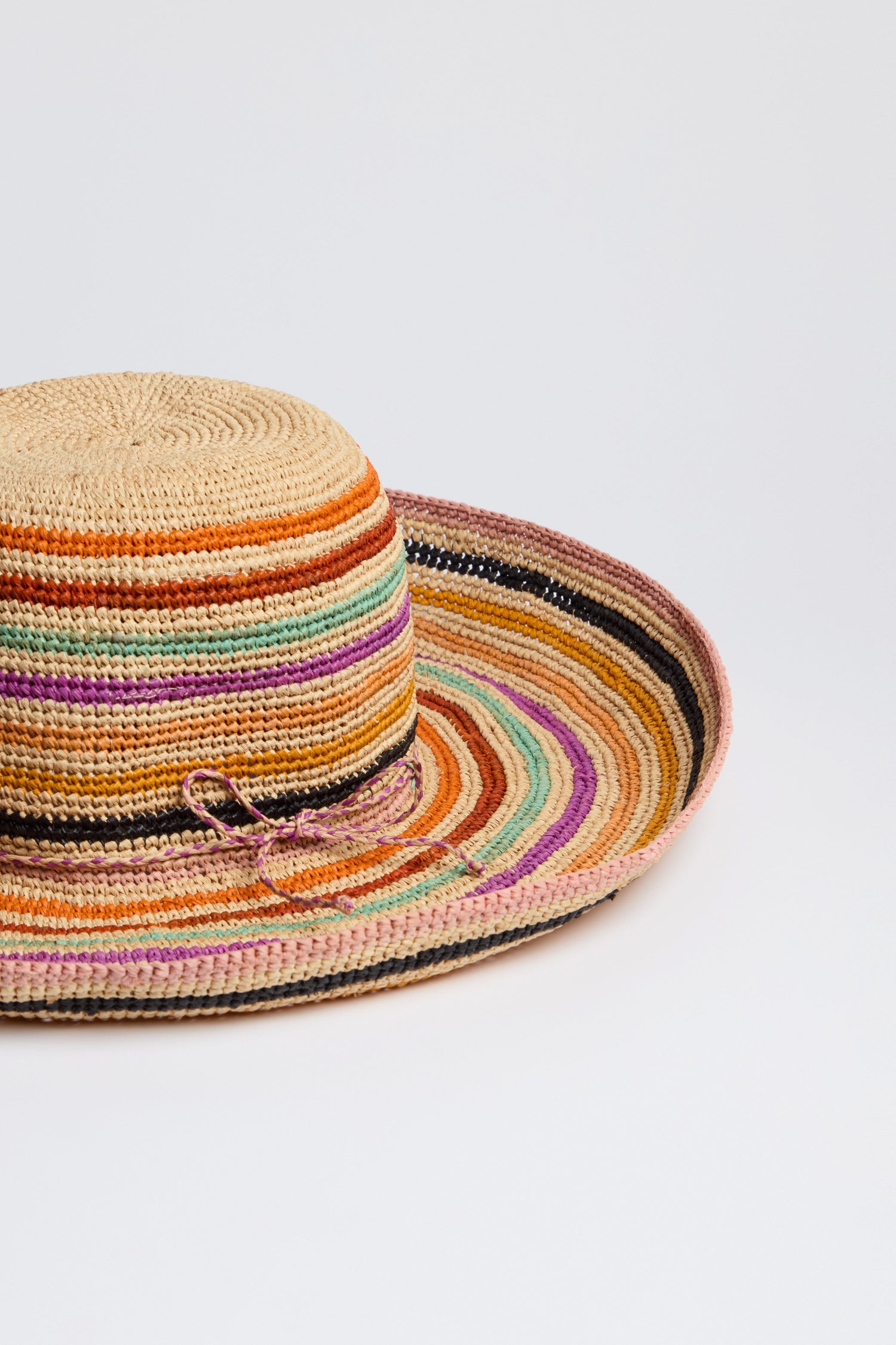 The Handwoven Rainbow Stripe Raffia Hat showcases a wide-brim design with horizontal rainbow stripes on a white background, exuding artisanal charm and boho-chic style.