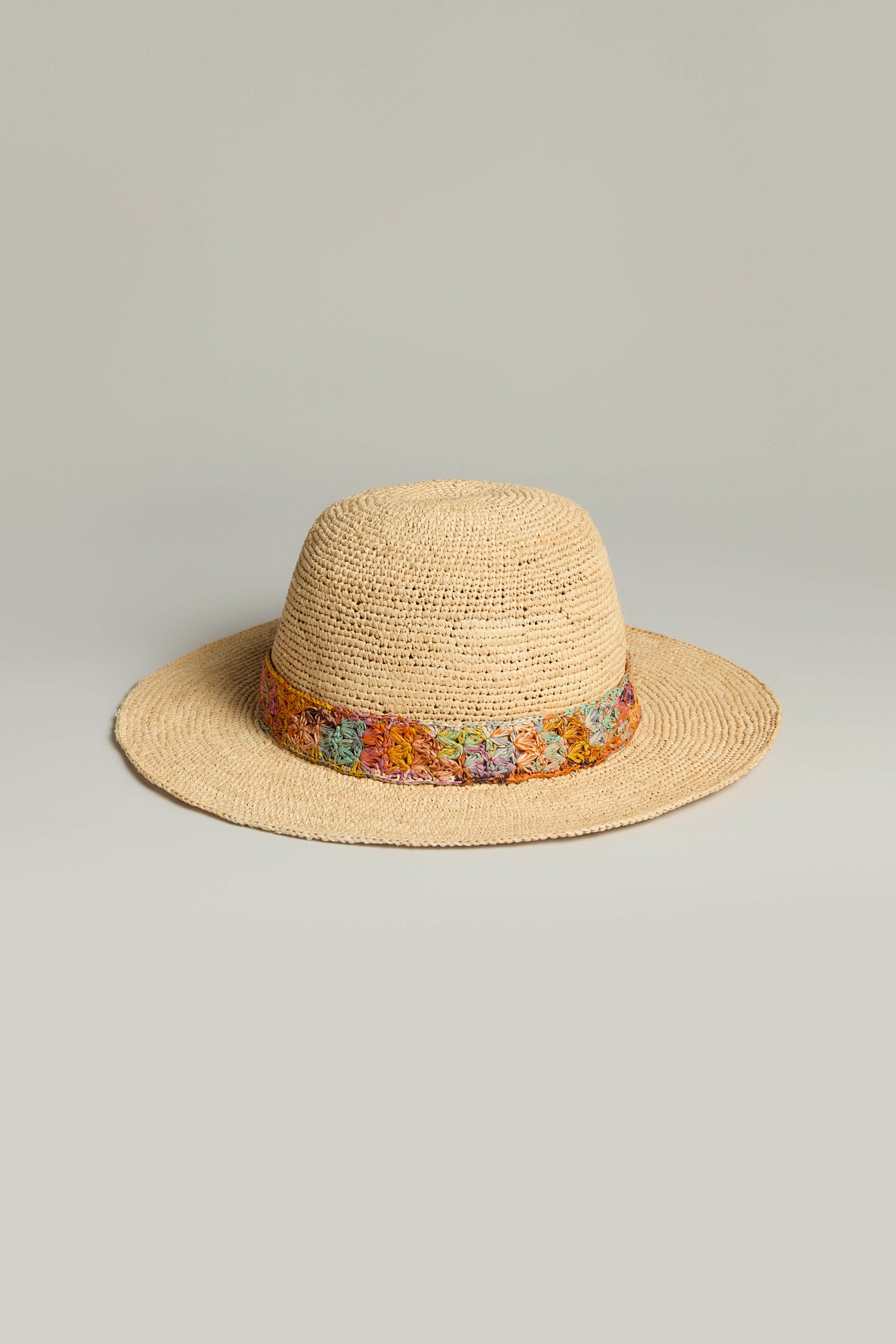 The Handwoven Flower Raffia Hat features a beige wide brim for sun protection and a vibrant floral band on the crown, elegantly highlighting sustainable fashion.