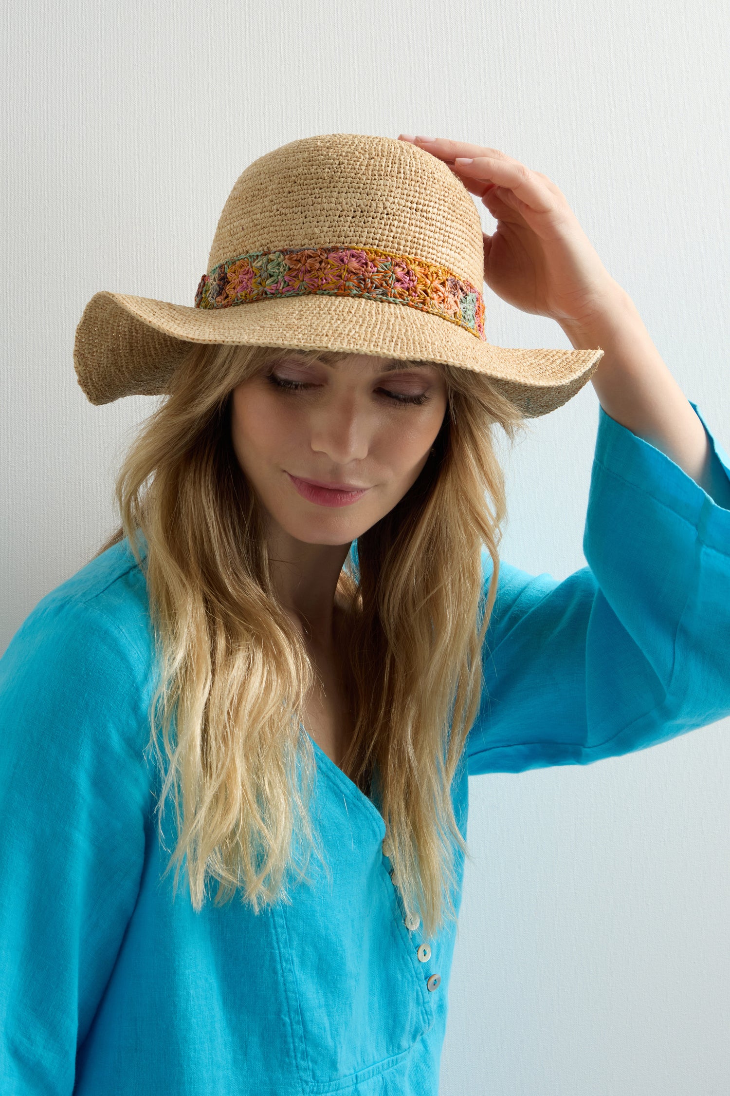 Wearing a Handwoven Flower Raffia Hat and a blue blouse, the person stands against a neutral background, effortlessly blending style with sun protection.