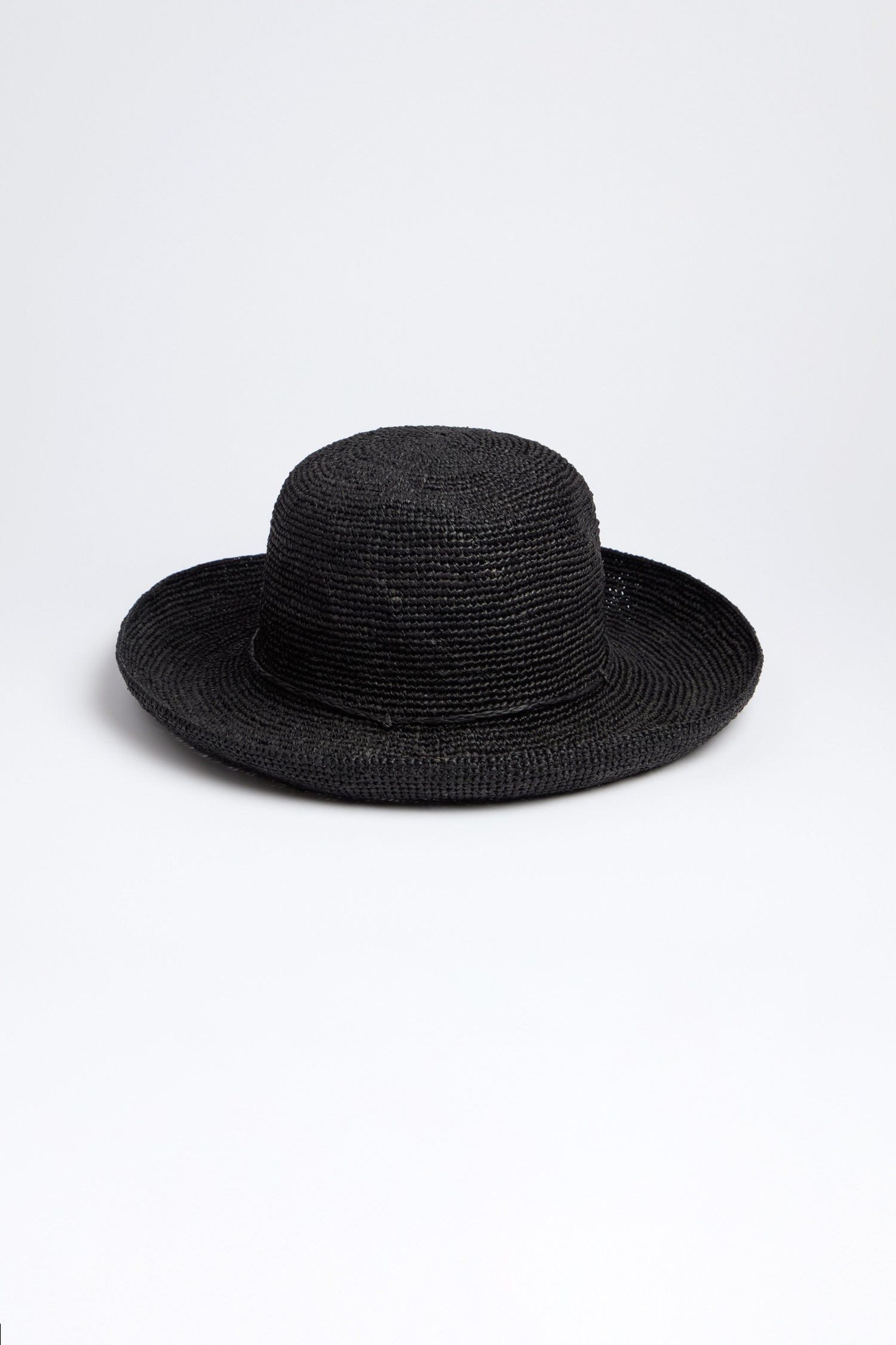 The Rabarany Handwoven Raffia Hat is a black straw hat with a wide brim and rounded crown, expertly crafted using Madagascar weaving techniques. Displayed on a plain white background, it highlights its lightweight and breathable design.