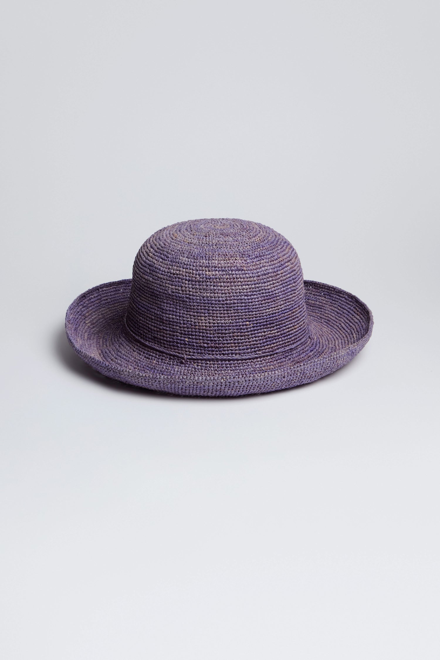 The Handwoven Raffia Hat, crafted in Madagascar, boasts a wide brim and a lovely purple hue, sitting elegantly on any surface.