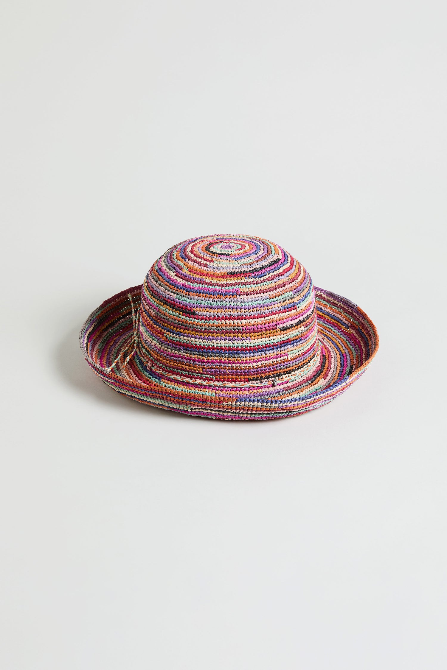 The Handwoven Rainbow Raffia Hat, crafted by artisans in Madagascar, showcases a multicolored design with a round crown and upturned brim, displayed against a plain white background.