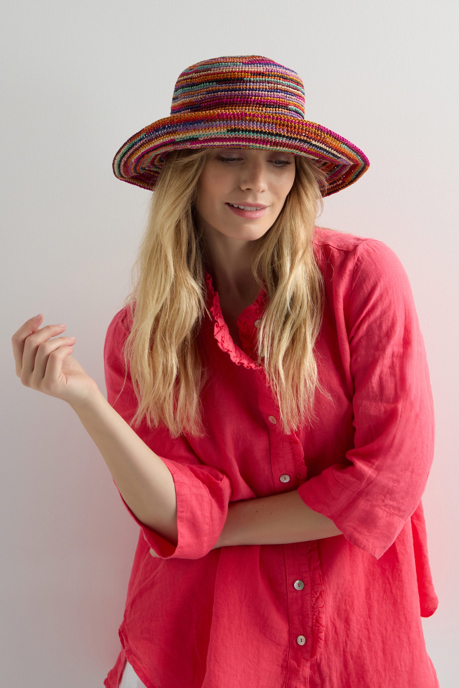 A woman in a pink shirt smiles gently as she wears the chic Handwoven Rainbow Raffia Hat, offering stylish sun protection against the stark white background.