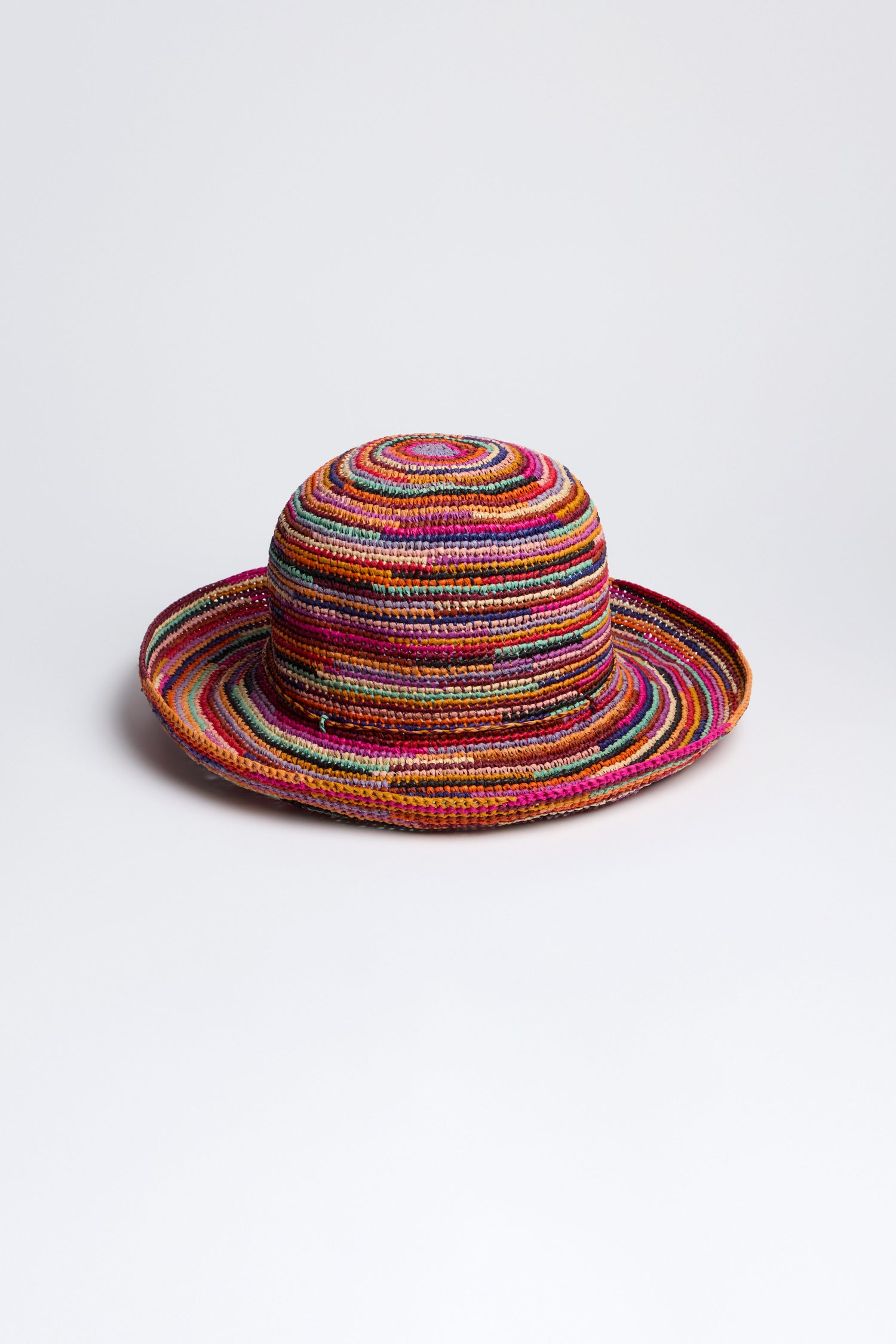 The Handwoven Rainbow Raffia Hat features a vibrant, wide round brim and dome-shaped crown with a multicolored pattern of concentric circles, offering chic sun protection.