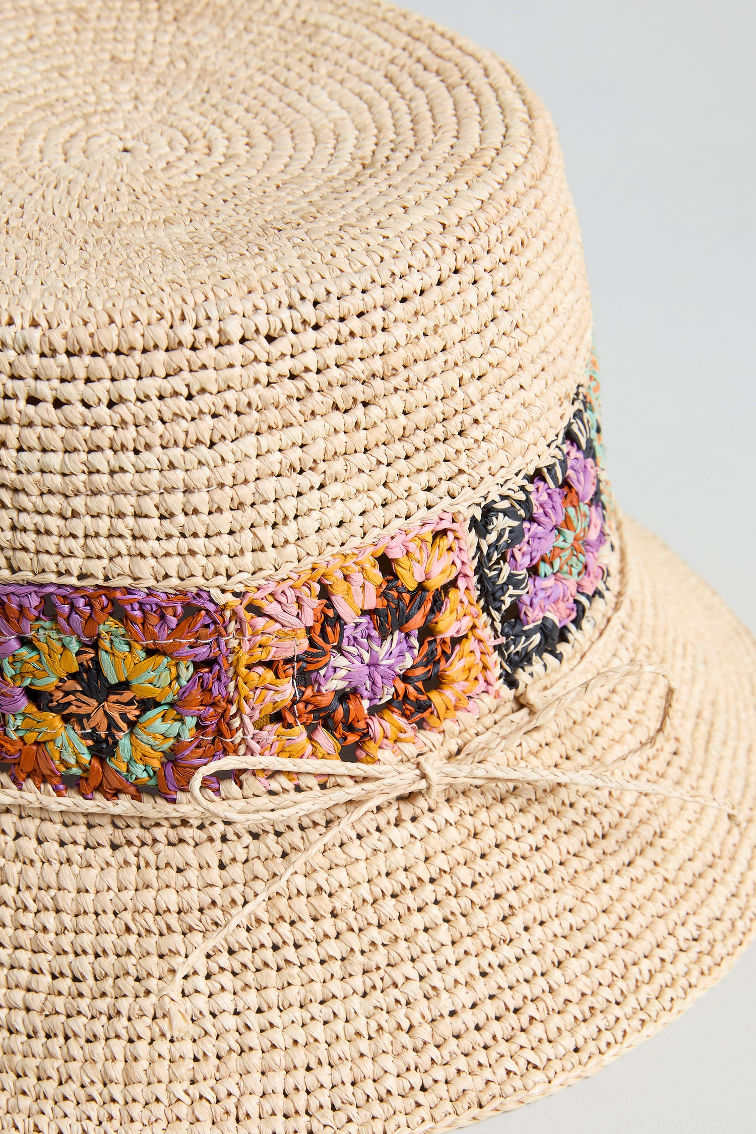 Close-up of the Handwoven Raffia Flower Bucket Hat from Madagascar, featuring a vibrant embroidered band and a slim straw tie at the crown’s base.