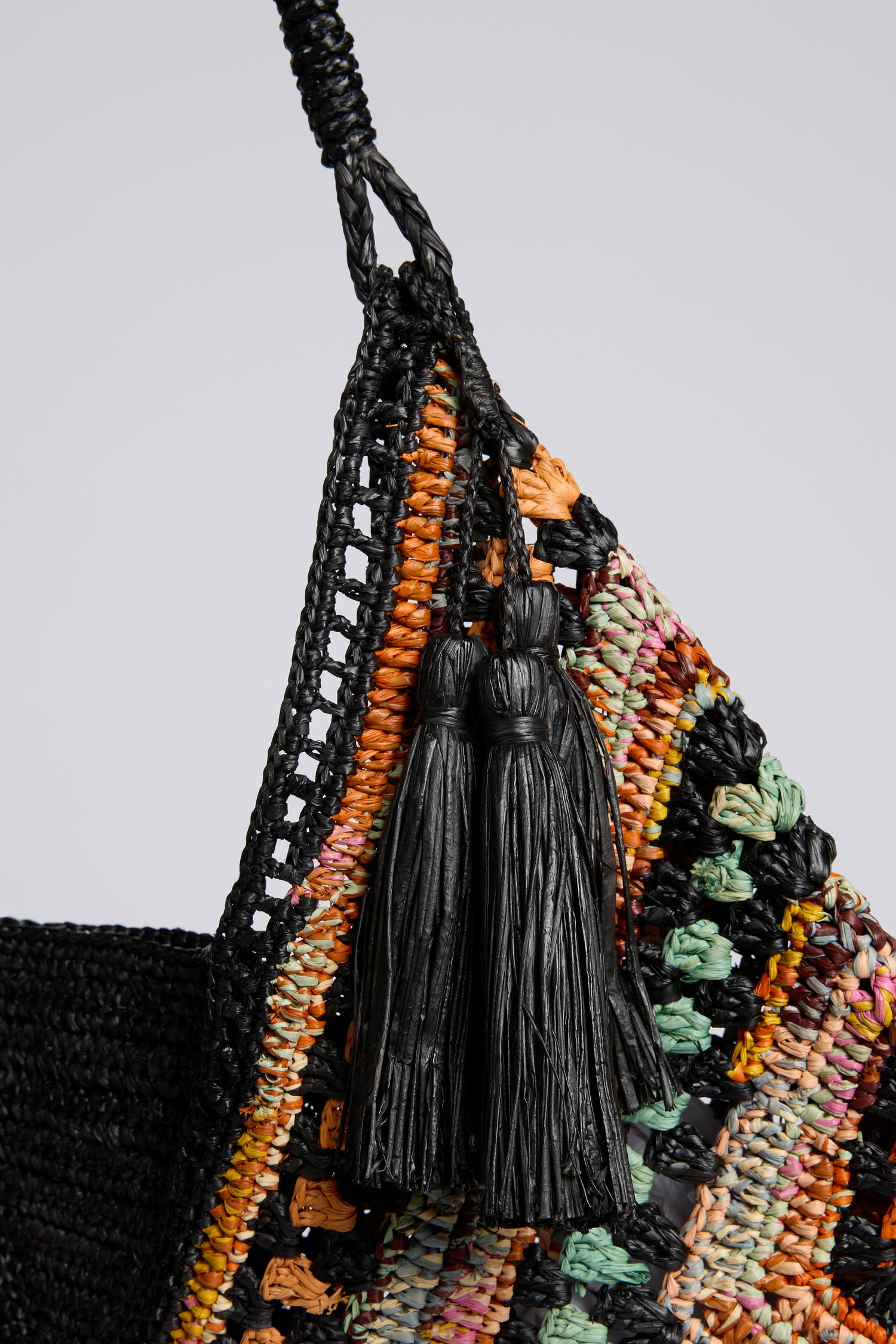 Close-up of the Handwoven Bohemian Raffia Bag, showcasing a vibrant geometric patchwork design and two black tassels dangling from the strap.