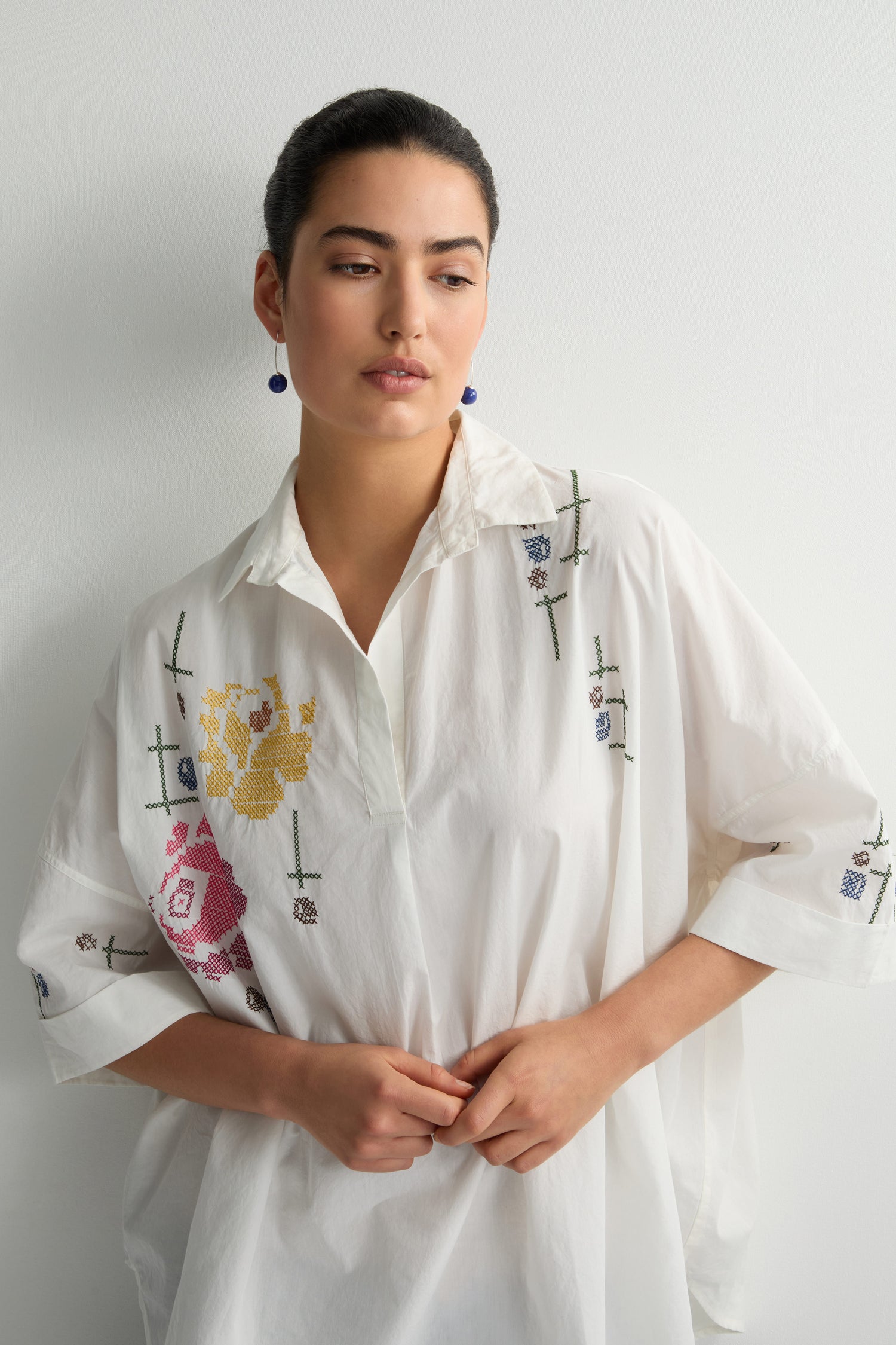 A person stands against a white background, wearing the Cross Stitch Embroidery Tunic, featuring delicate cross stitch detailing.