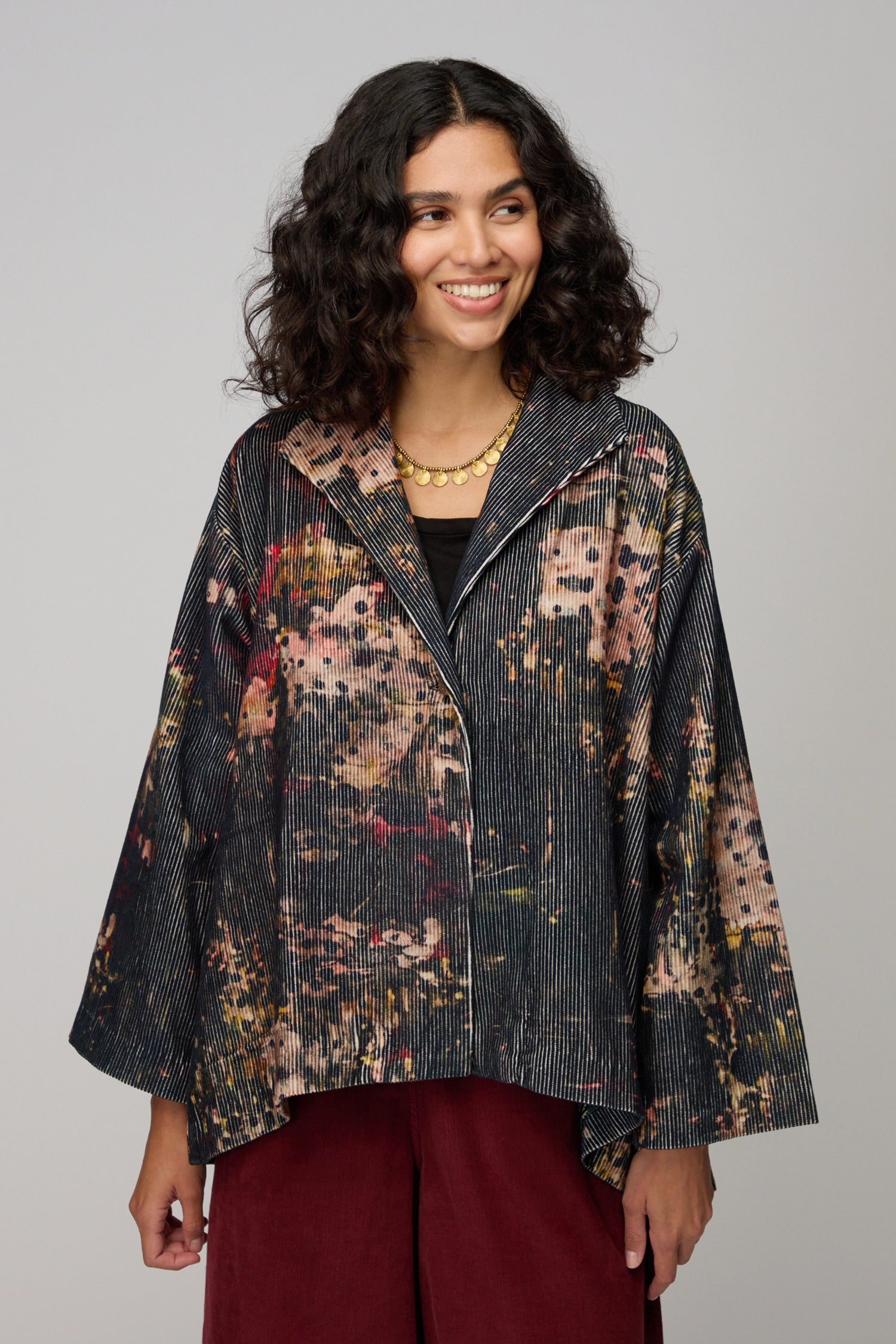 Woman wearing a Print Corduroy Jacket with a relaxed fit over a black top and dark red pants, standing against a plain background.